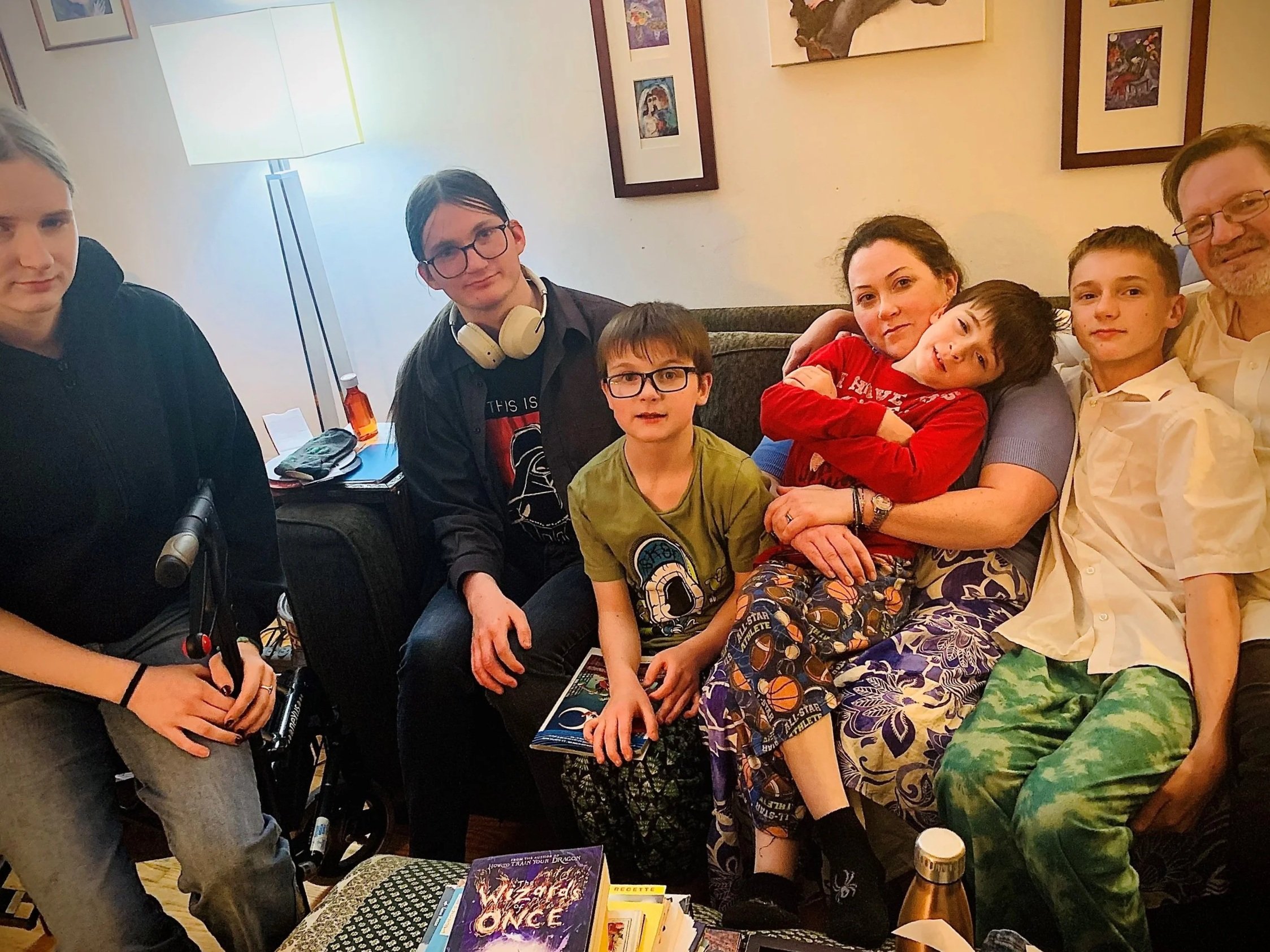 Family gathered in living room posing together for a photo, with artwork on the wall and books on a coffee table.