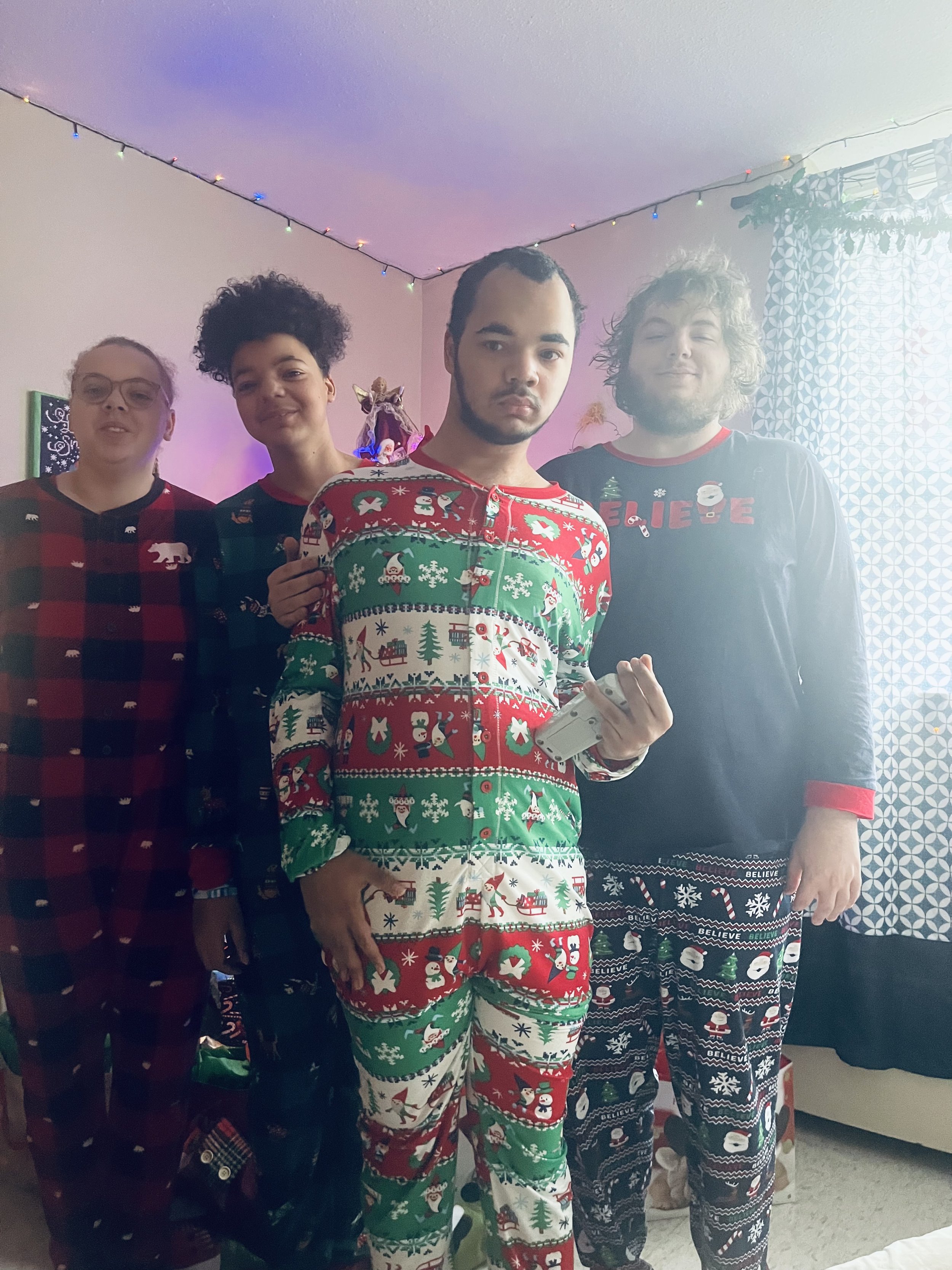 Four people standing together in pajamas with Christmas and holiday-themed patterns in a decorated room.