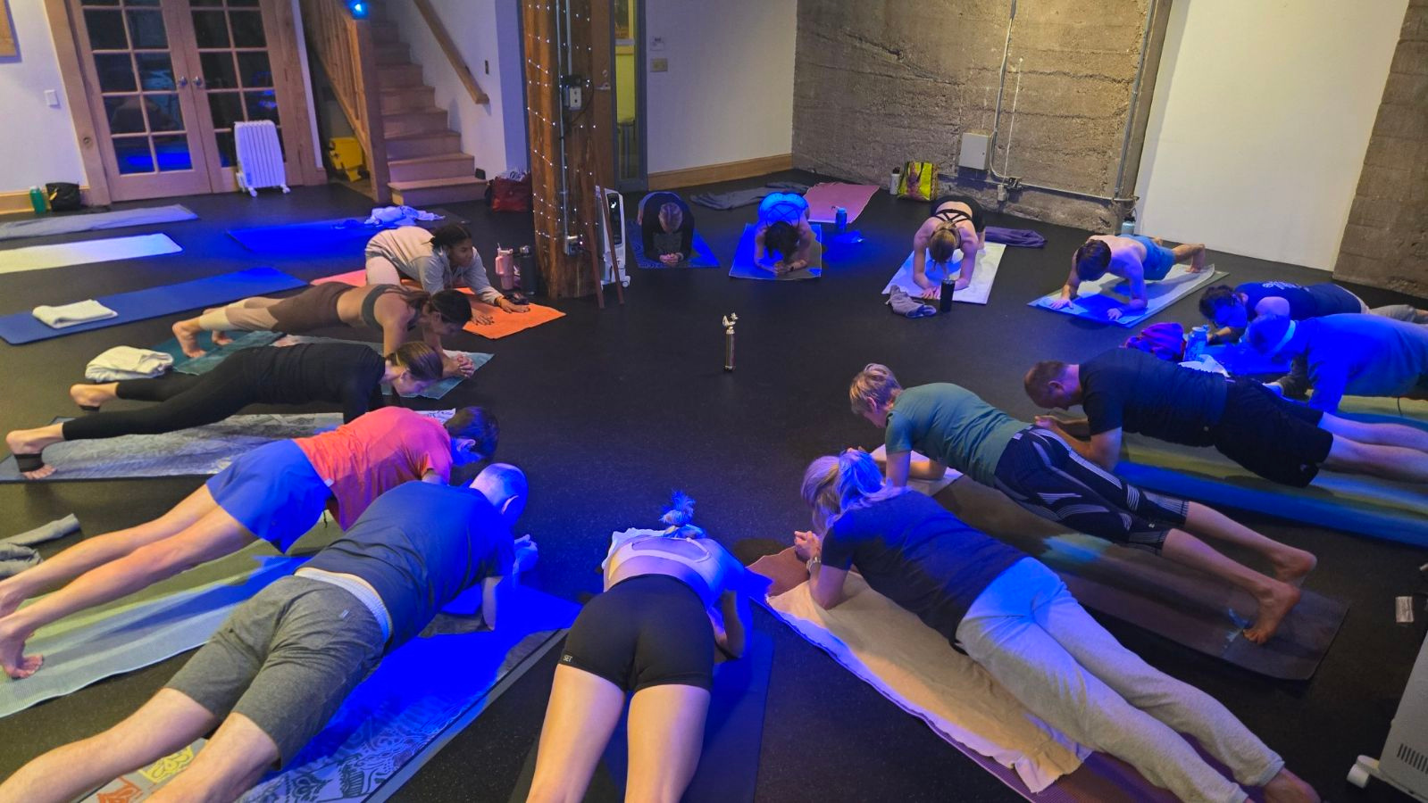 Group of people participating in a yoga class, doing plank poses on their mats in a dimly lit studio.