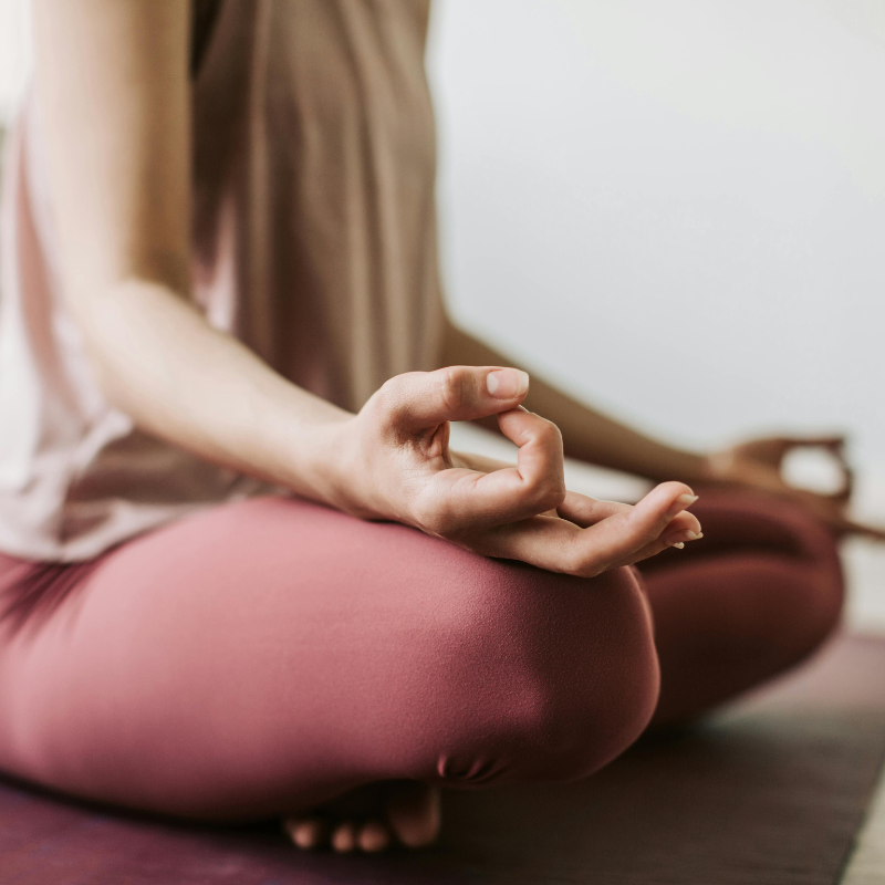 Person practicing meditation in seated yoga pose with hand in Gyan mudra, on a yoga mat.