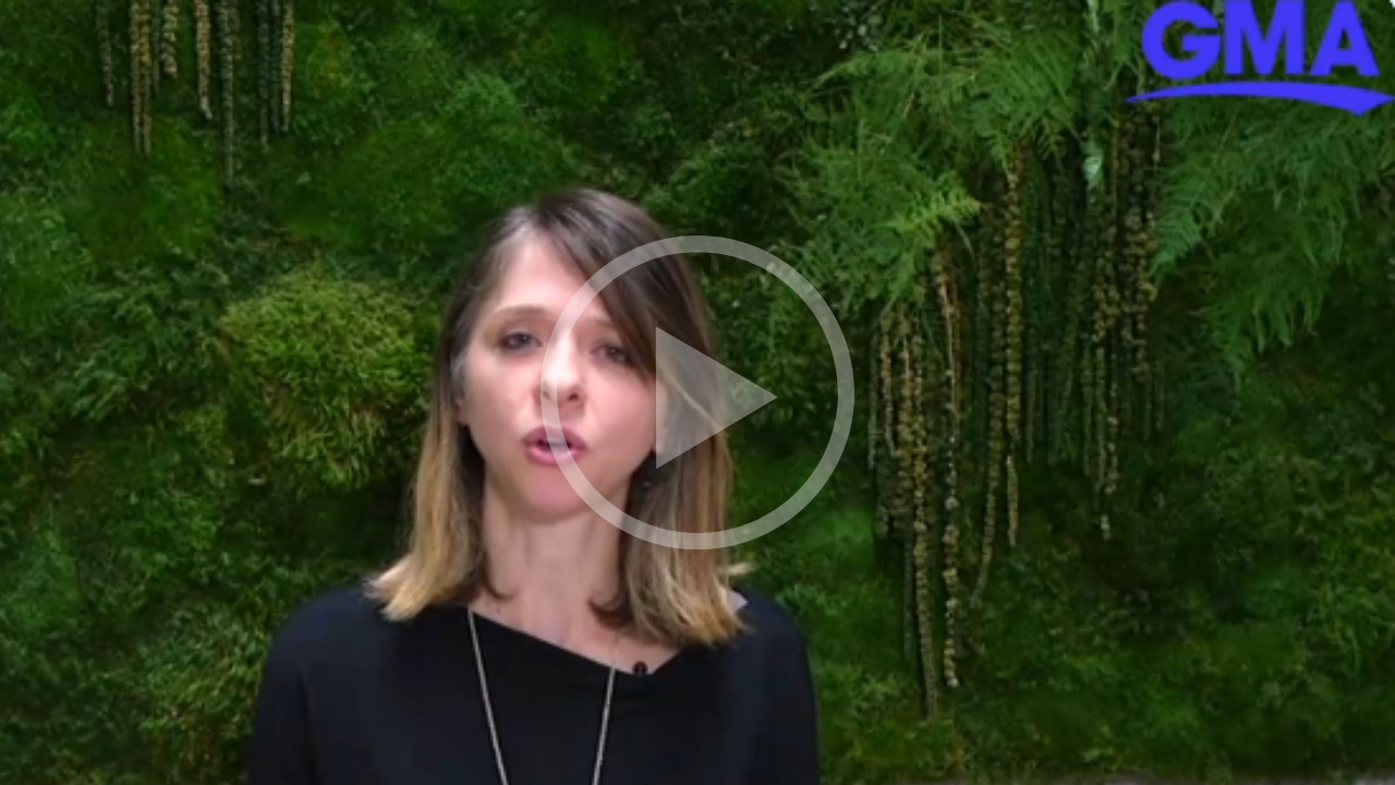 A woman with shoulder-length brown hair speaking in front of a green, leafy background with plants and ferns, during a video segment for GMA.