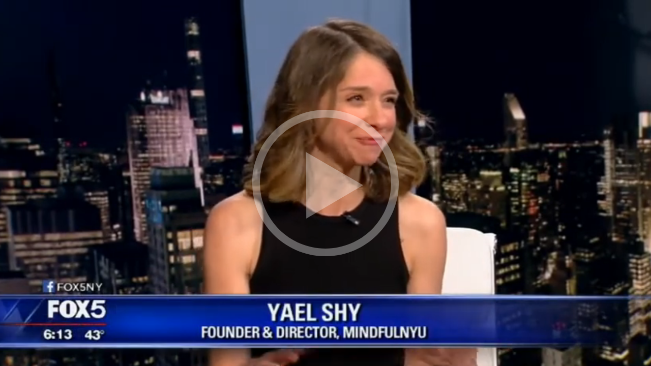 A woman with shoulder-length light brown hair in a black sleeveless top, sitting on a TV set with a city skyline backdrop, during a FOX5 interview. Text overlay identifies her as Yael Shy, founder and director of MindfulNYU, at 6:13 with 43°F.