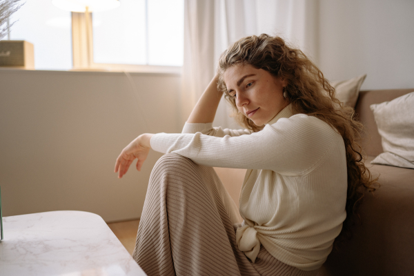 A woman sitting on the floor in a room, appearing sad or contemplative, with her hand resting on her head.