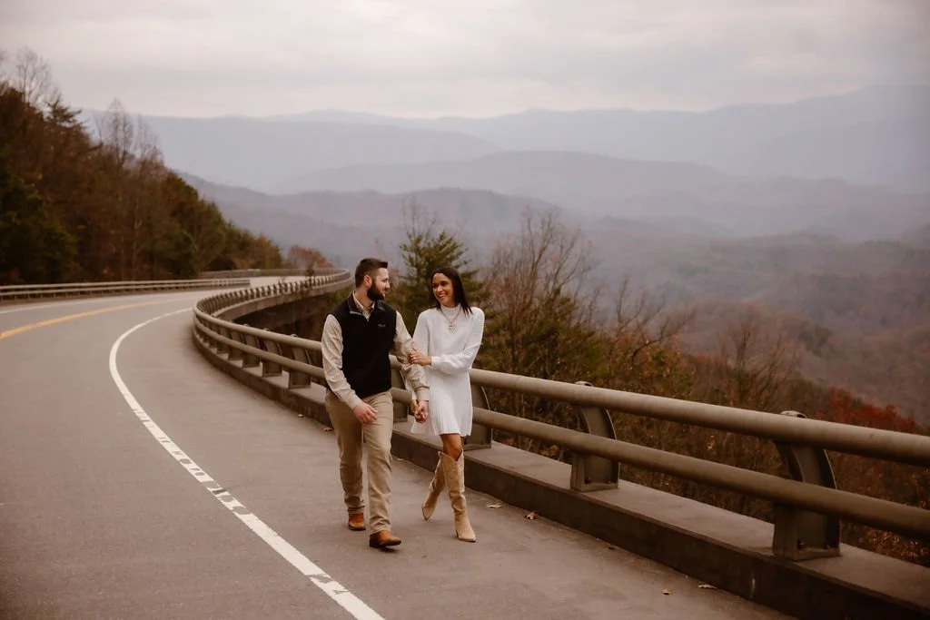 Couple walking along Foothills Parkway scenic road with mountain views, wearing coordinated neutral engagement photos clothes captured by Gatlinburg photographer during fall session