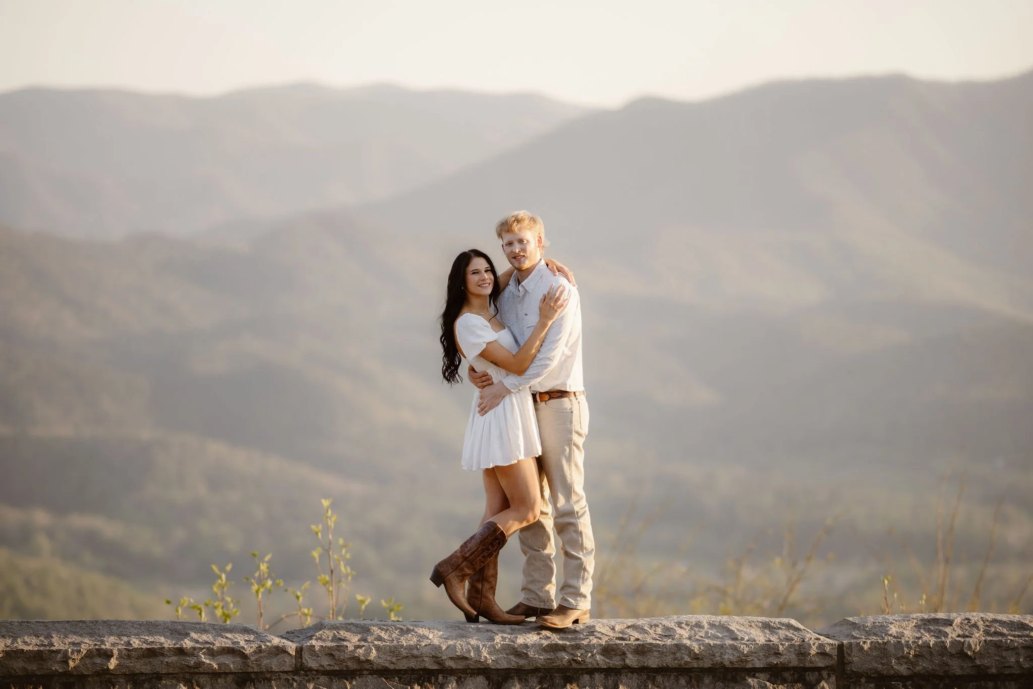 Engaged couple embracing at a scenic overlook along Foothills Parkway with the Smoky Mountains in the background during a sunset engagement session.