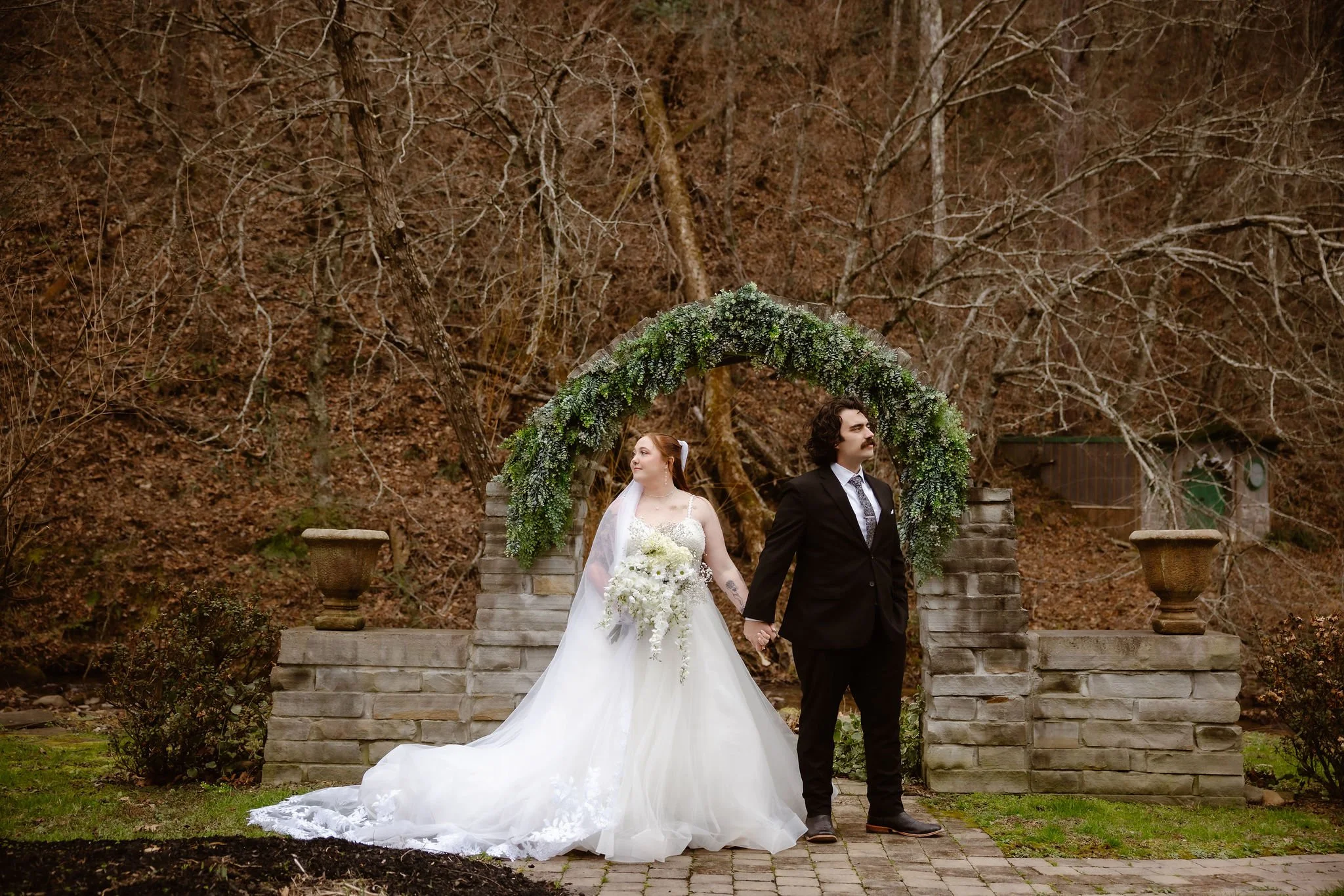 Bride and groom holding hands beneath a greenery-covered stone arch during a romantic micro wedding ceremony in the Smoky Mountains, captured by a Gatlinburg elopement photographer.