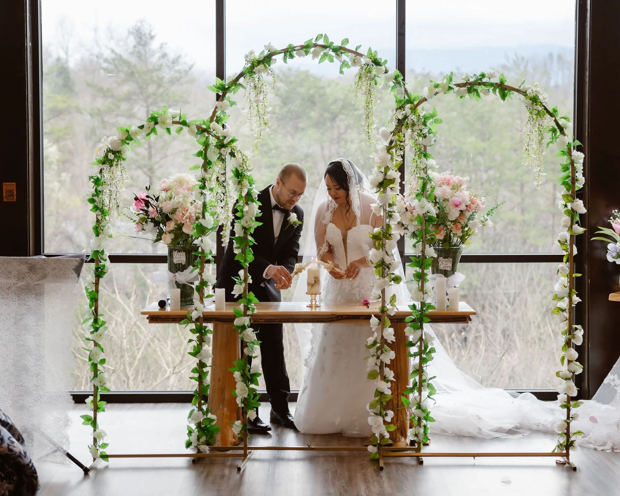 Bride and groom lighting a unity candle beneath a floral ceremony arch during an Indoor elopement at a Wild Briar Lodge Wedding, photographed by a Gatlinburg photographer.