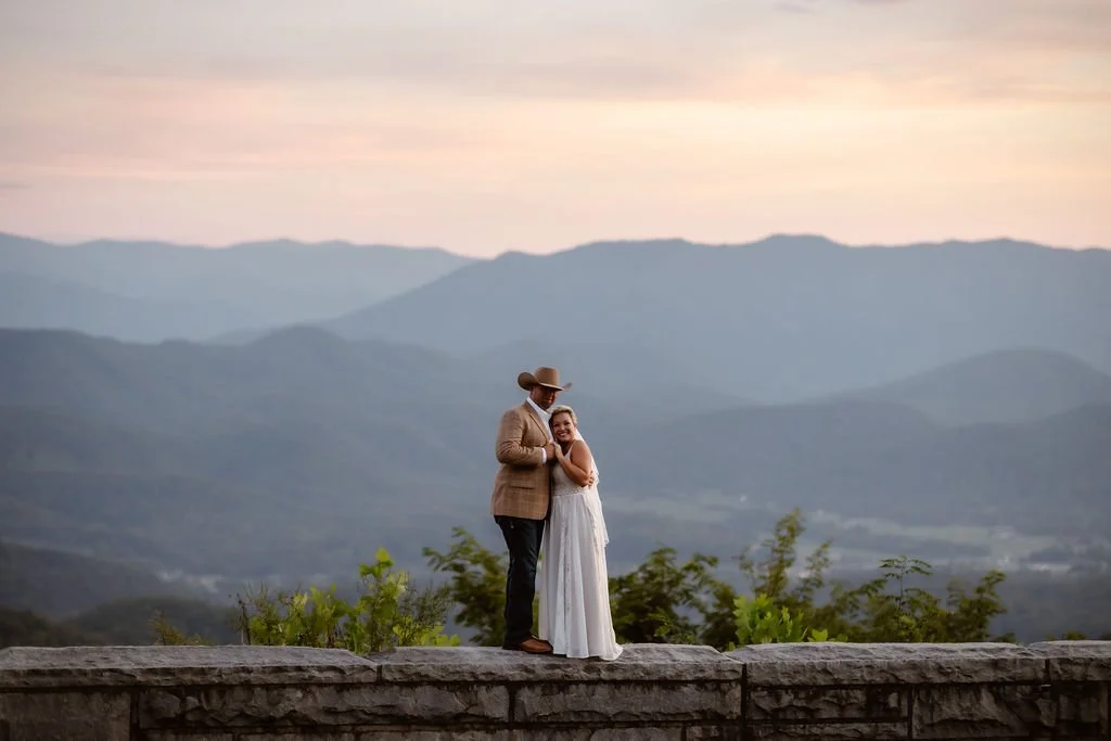 Wide scenic portrait of the bride and groom embracing on a stone overlook during their sunset elopement at Foothills Parkway, with layered Smoky Mountains views highlighting their Smoky Mountain elopement.