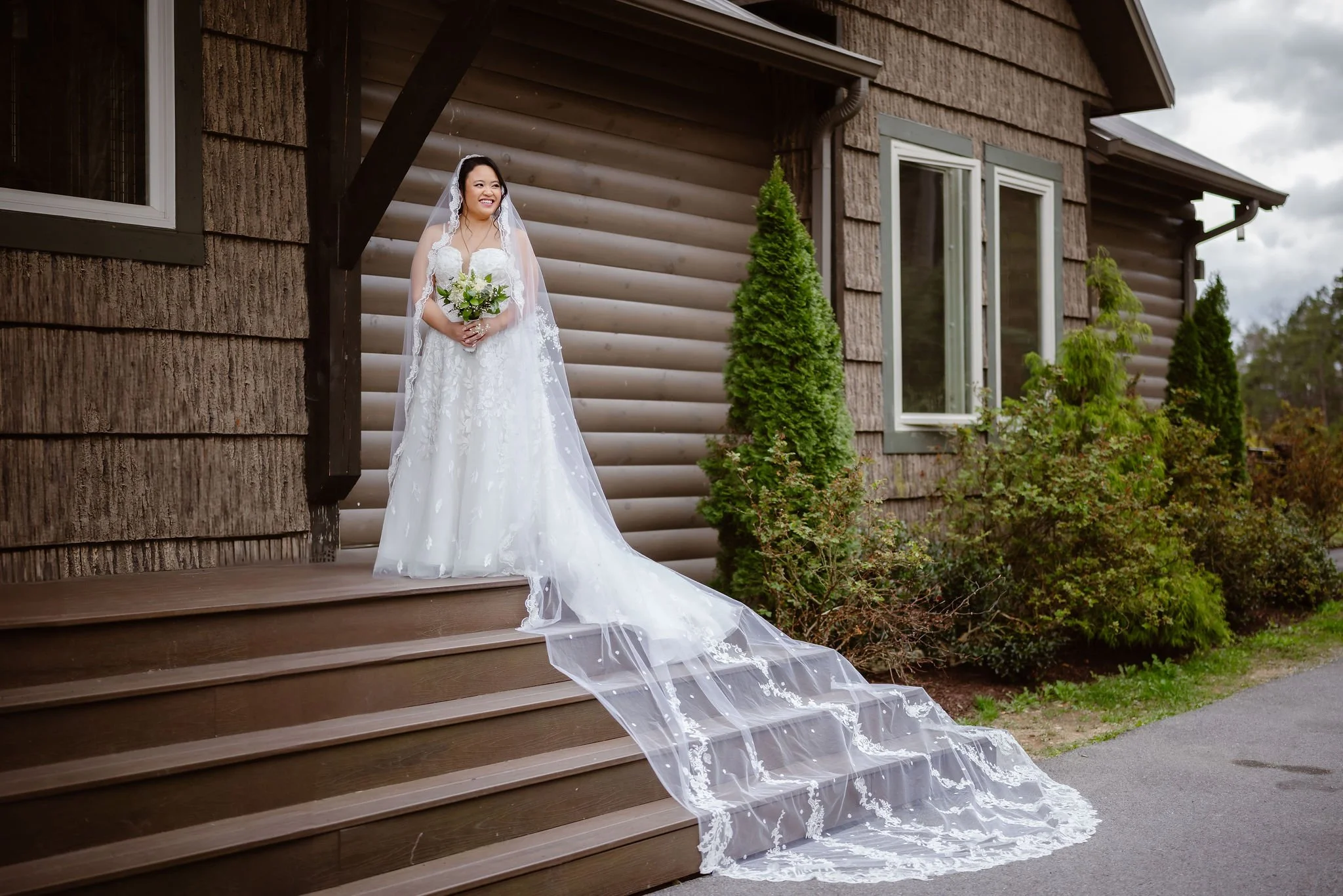 Bride stands on the porch outside a Wild Briar Lodge Wedding, showcasing her lace cathedral veil and bouquet before her Indoor elopement, photographed by a Gatlinburg photographer.