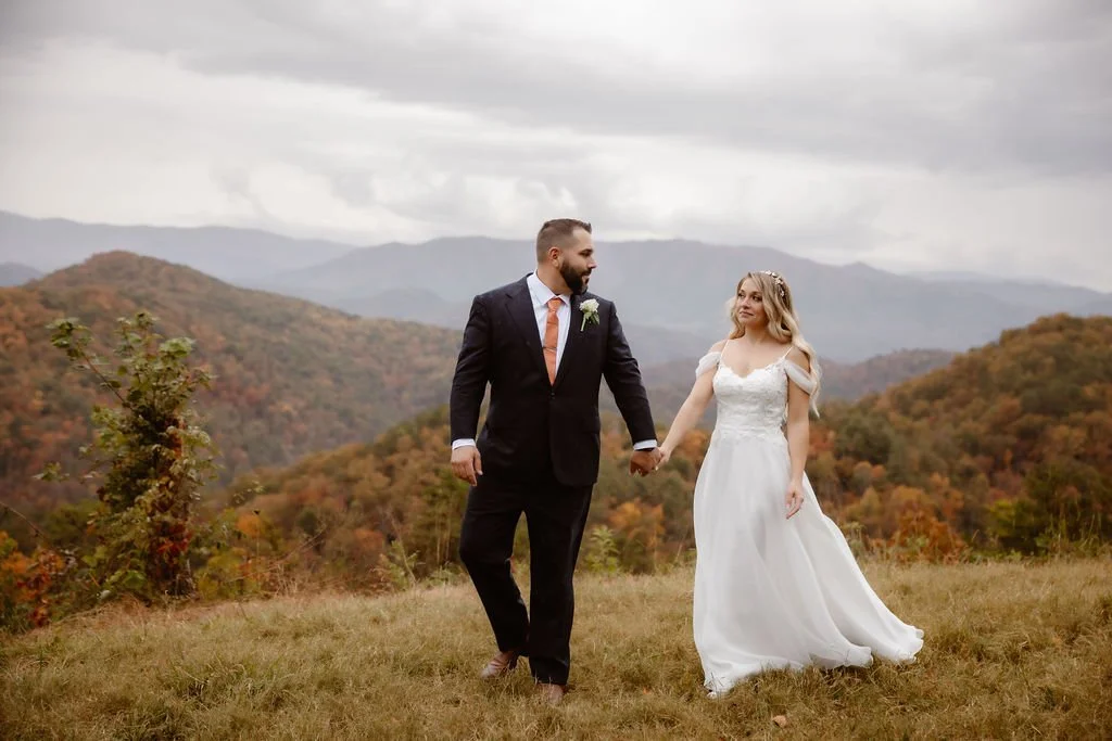 Hand in hand, the newlyweds walk along the ridge with the misty Smoky Mountains behind them—surrounded by autumn’s rich colors and wrapped in the quiet romance of their Gatlinburg micro wedding on Foothills Parkway.