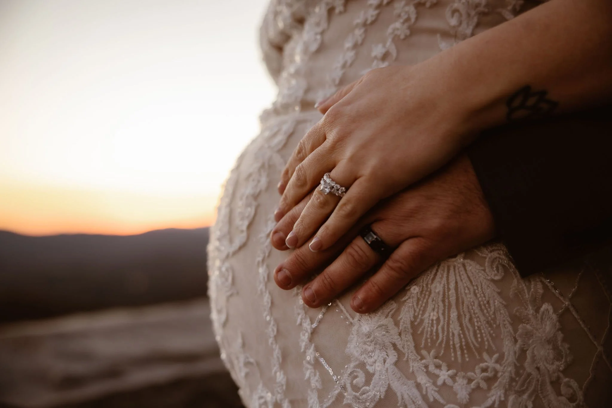Close-up of a pregnant bride and groom holding hands over a lace wedding dress at sunset during pregnant wedding pictures in the Smoky Mountains, captured by a Gatlinburg wedding photographer.