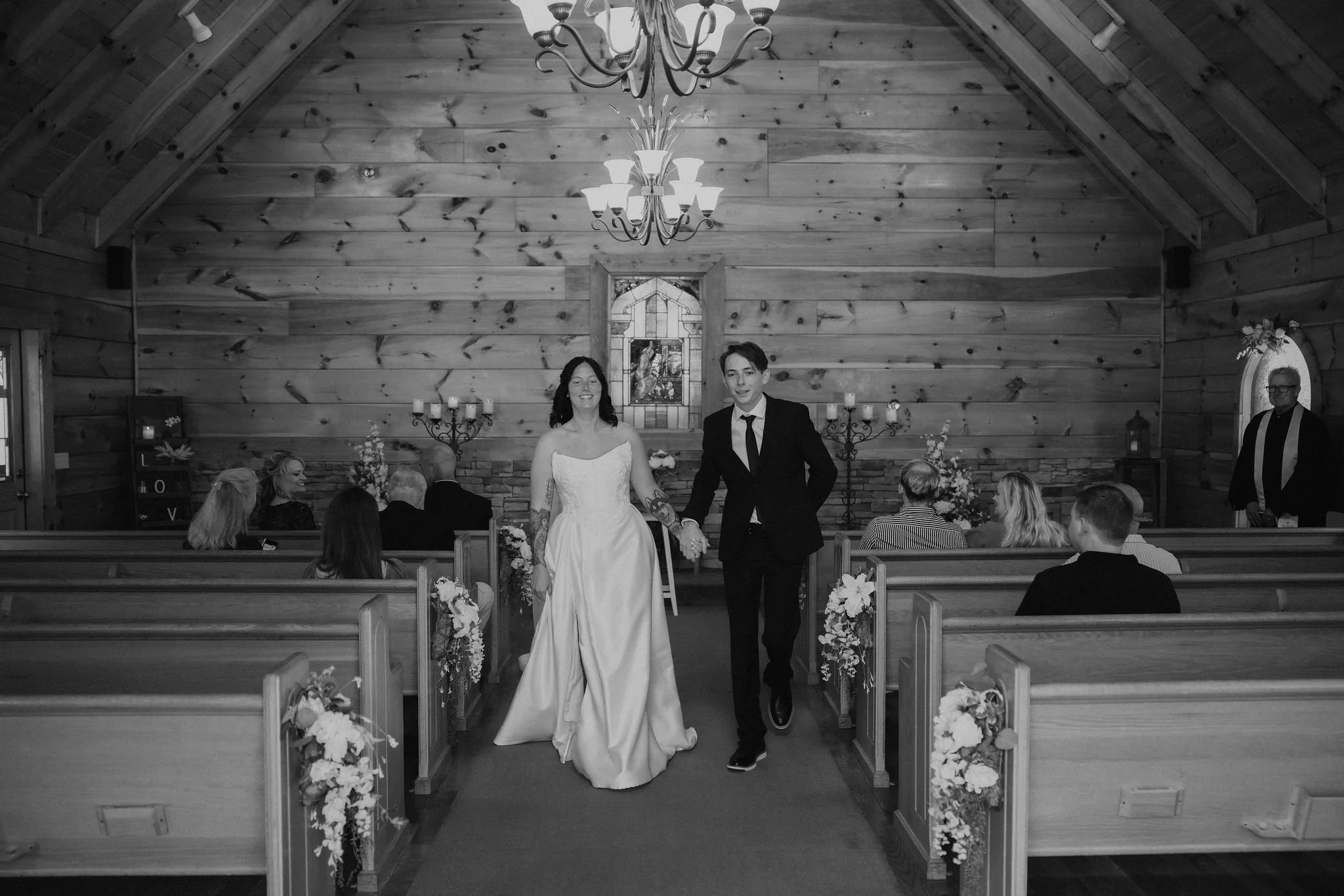 Newlyweds walk hand in hand down the aisle after their Gatlinburg elopement ceremony inside the wood-paneled Little Log Chapel in Gatlinburg.