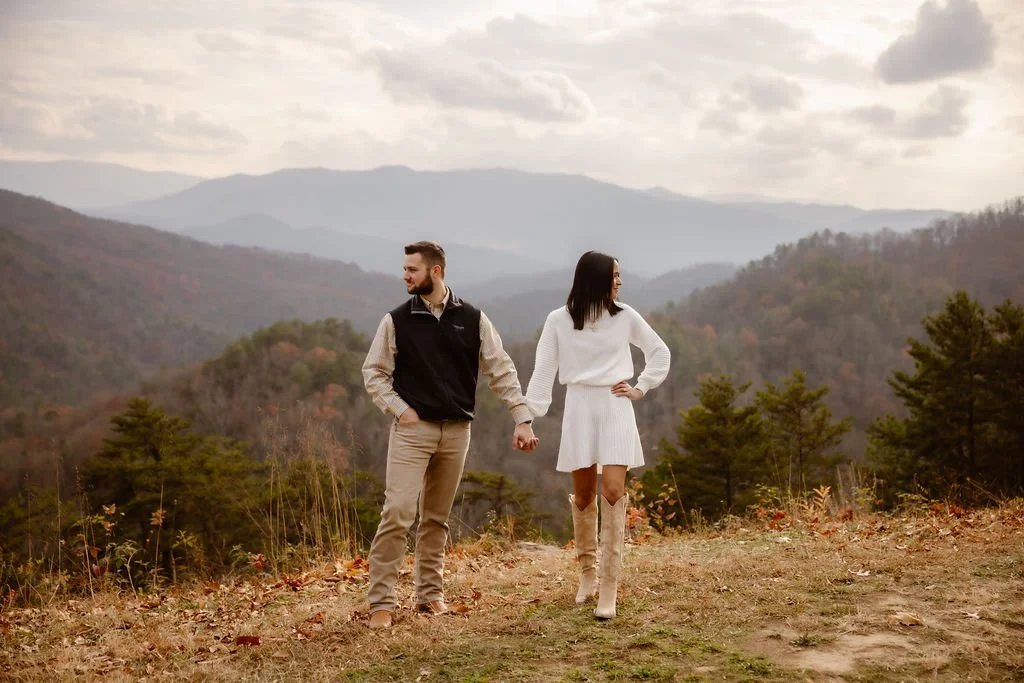 Couple holding hands at Foothills Parkway overlook with mountain views, styled engagement photos clothes featuring neutral fall outfits captured by Gatlinburg photographer during scenic engagement session