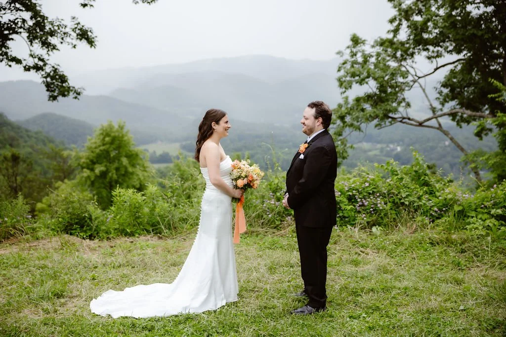 Bride and groom facing each other on a grassy overlook with misty mountain views in the background, surrounded by spring greenery and wildflowers—an elegant scene from Smoky Mountain Elopements in the Spring, captured by a Gatlinburg photographer.