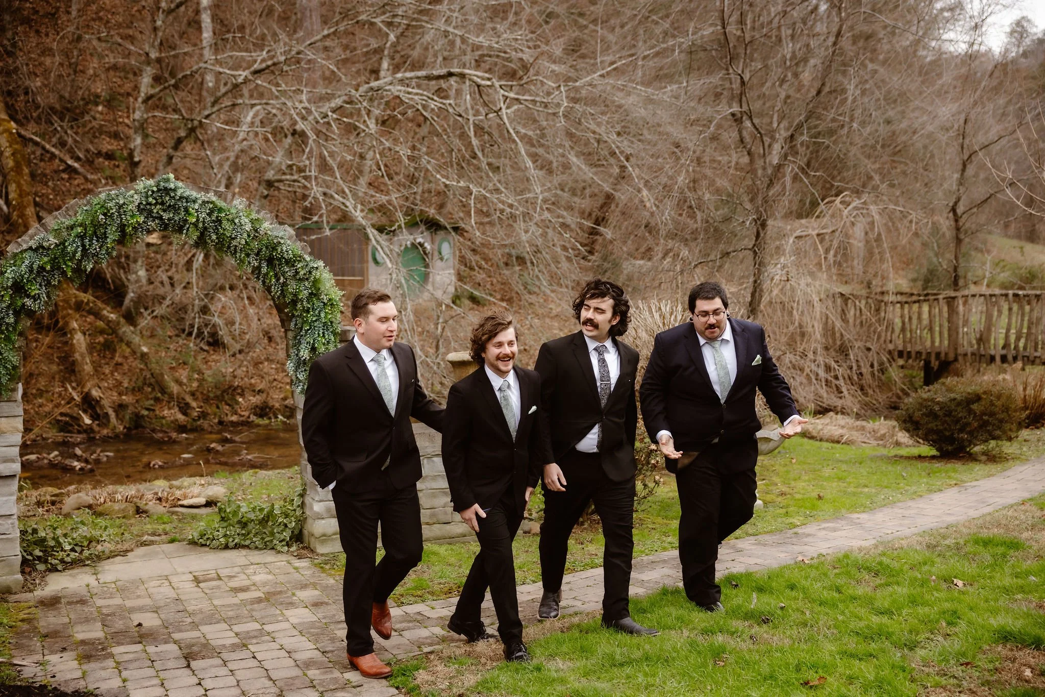 Groom and groomsmen walking together beside a creek and stone archway before a relaxed micro wedding celebration, captured by a Gatlinburg elopement photographer.