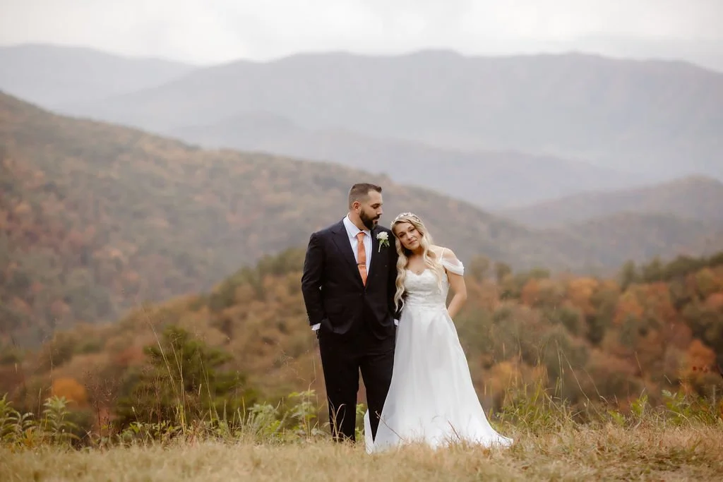 Bride and groom stand closely in front of a sweeping Smoky Mountain backdrop, framed by fall foliage, during their intimate Gatlinburg micro wedding on Foothills Parkway.