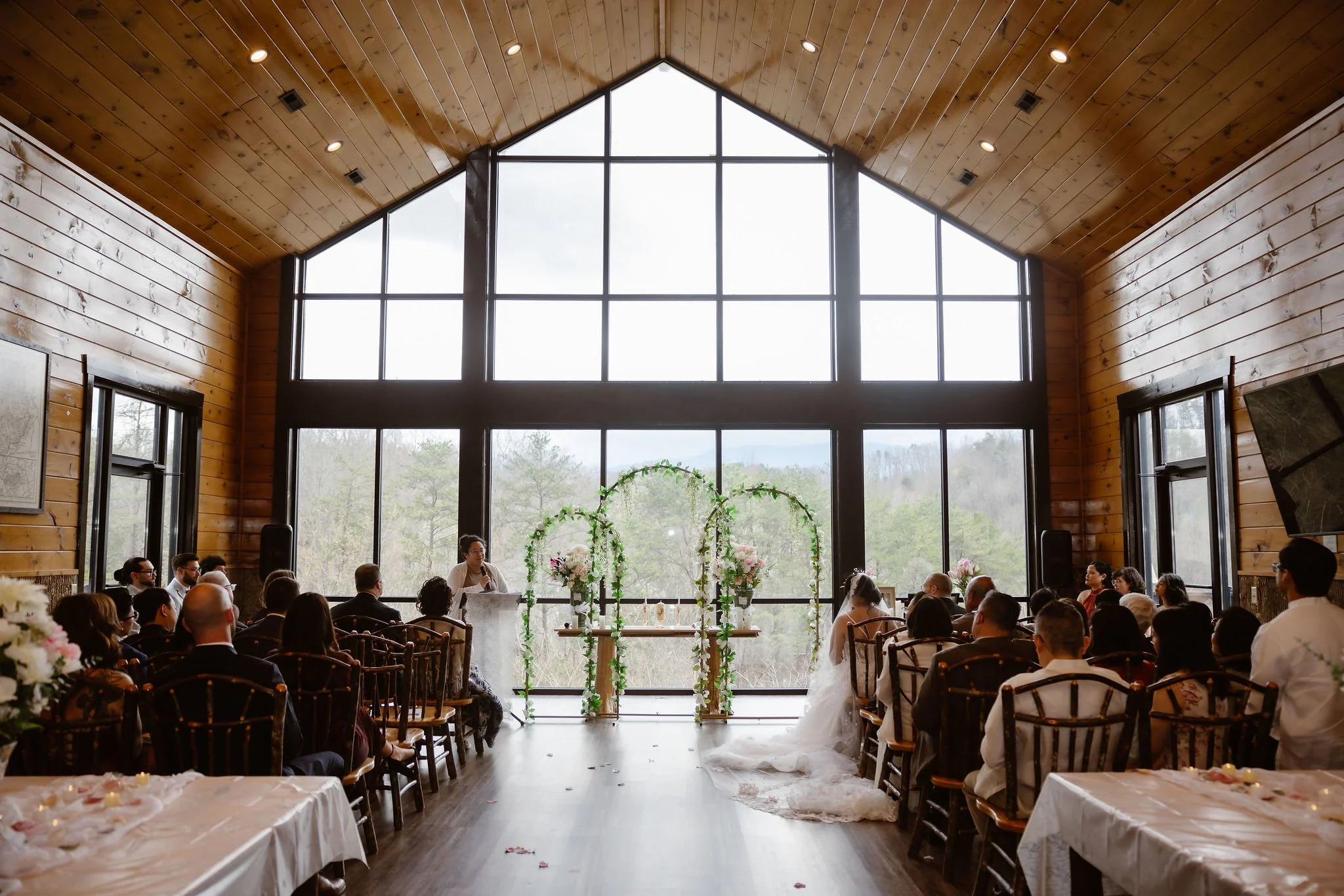 Wide view of guests gathered for an Indoor elopement ceremony at a Wild Briar Lodge Wedding, featuring floor-to-ceiling windows and mountain views, captured by a Gatlinburg photographer.