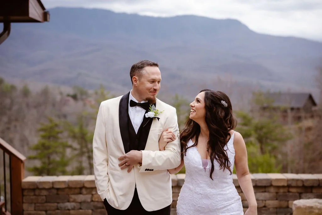 Newlywed couple walking arm in arm and smiling at each other with Smoky Mountain views in the background.