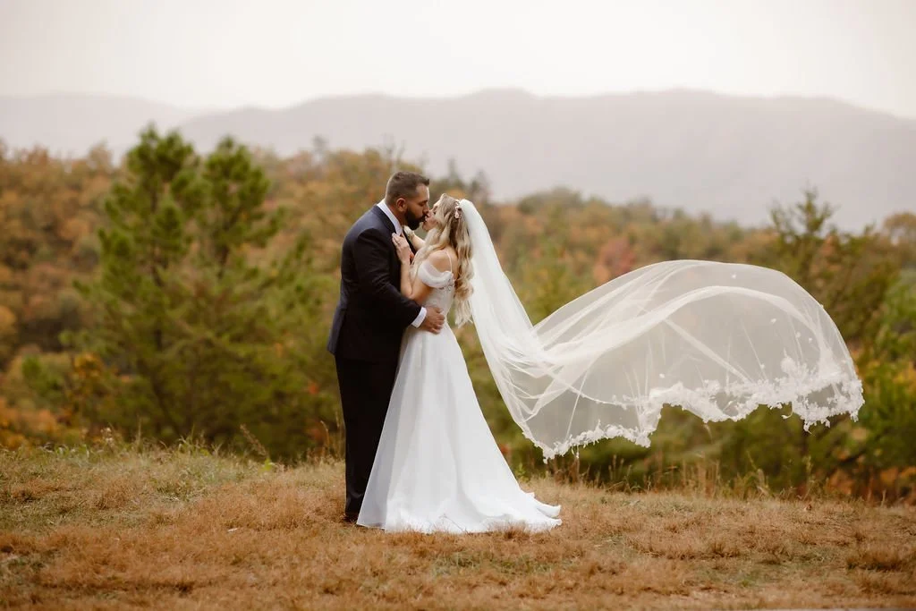 A dreamy kiss shared by the bride and groom as her veil floats in the mountain breeze—captured against the hazy ridges of the Smoky Mountains during their Foothills Parkway micro wedding. A perfect moment by their Gatlinburg photographer.