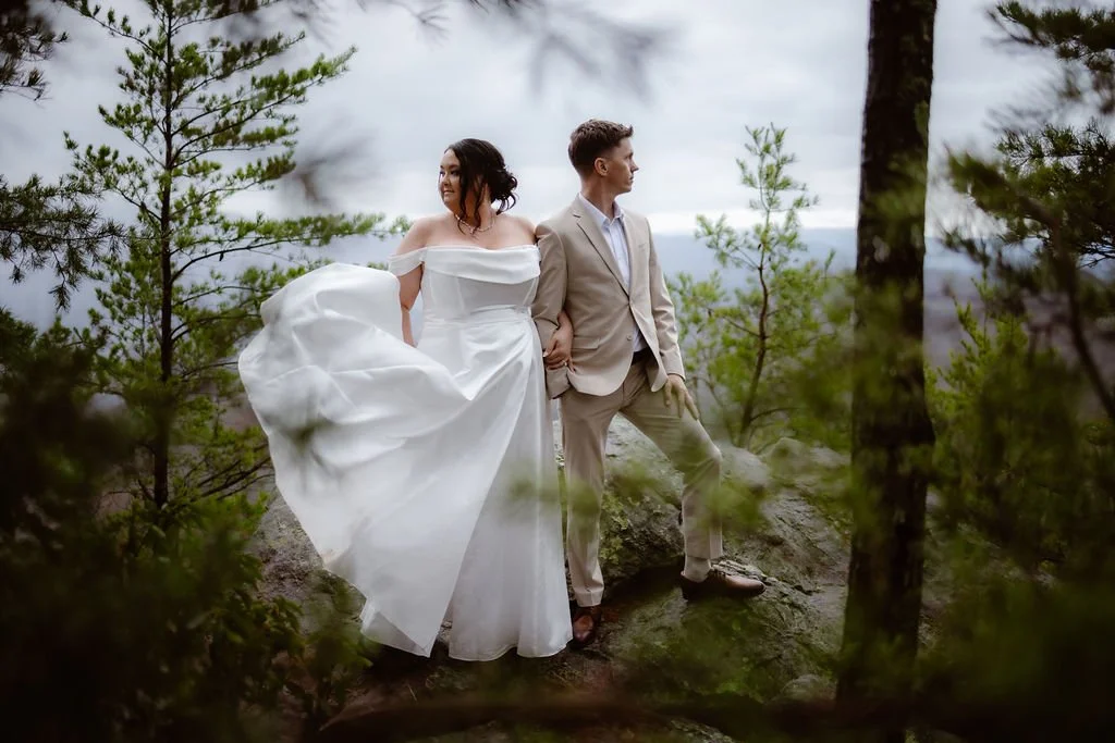 Couple holding hands on a rocky overlook during a forest elopement, with the bride's flowing gown and scenic mountain backdrop captured by a gatlinburg photographer for a foothills elopement