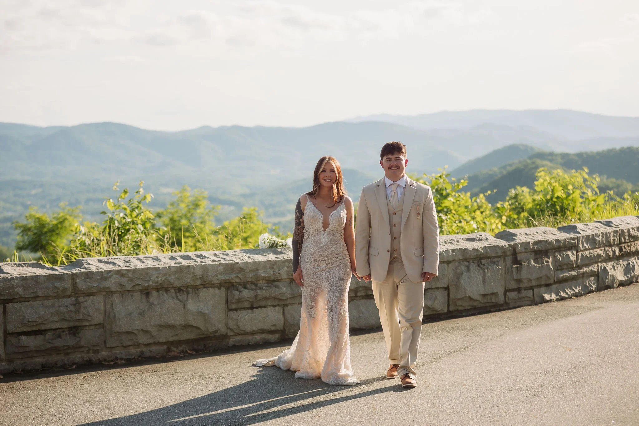 A newlywed couple walks hand in hand along Foothills Parkway in the warm afternoon sunlight, surrounded by panoramic mountain views during their romantic Gatlinburg elopement.
