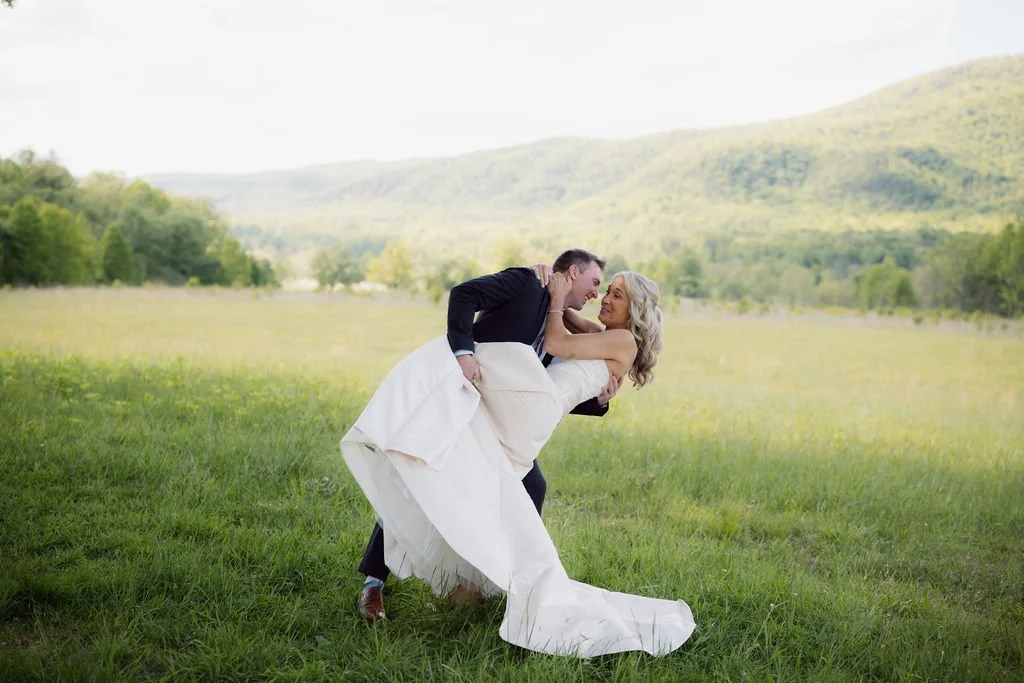 Groom playfully dips the bride in a grassy Cades Cove meadow, a candid portrait for couples considering eloping to Gatlinburg.