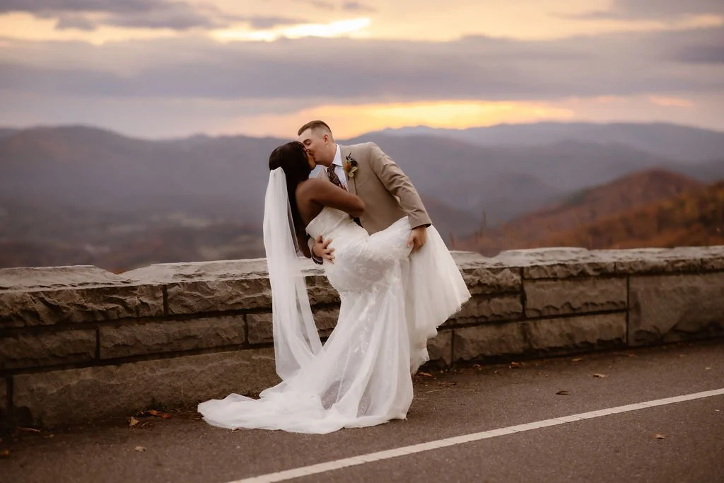 Groom dipping bride for a kiss at mountain overlook during sunset, foothills parkway elopement photography capturing romantic Smoky Mountains fall wedding with scenic views by a gatlinburg photographer specializing in outdoor elopements