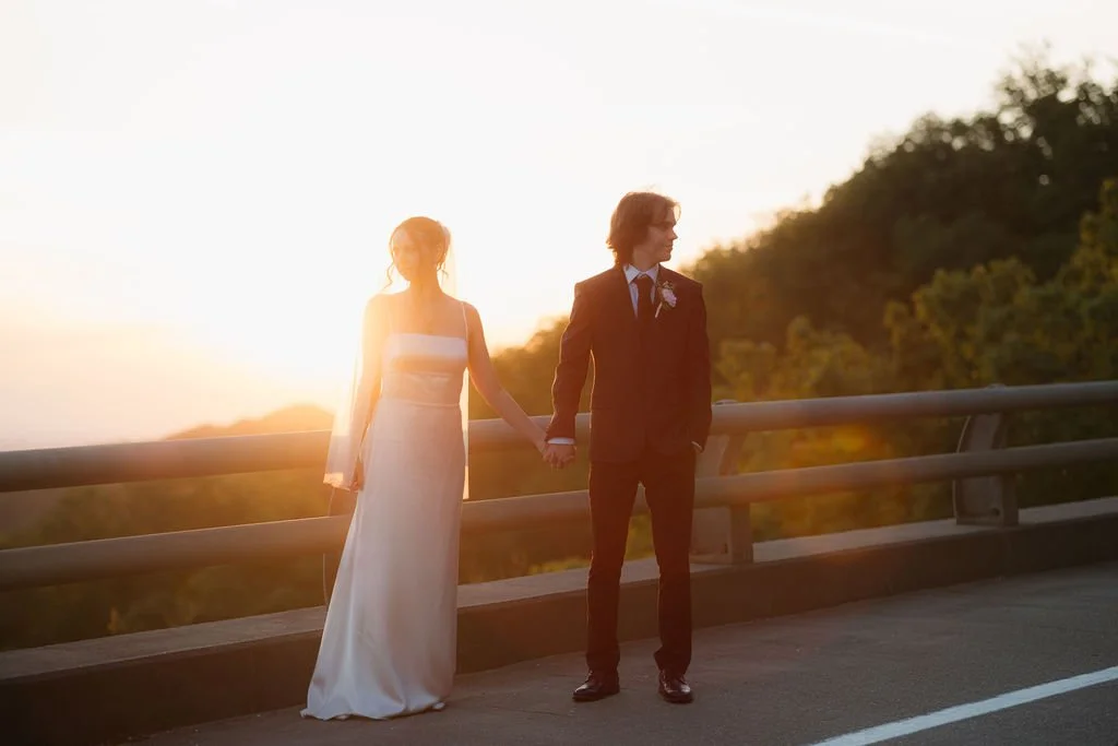 Newlyweds holding hands along the foothills parkway at sunset, surrounded by forested mountain views found along popular Gatlinburg scenic drives.