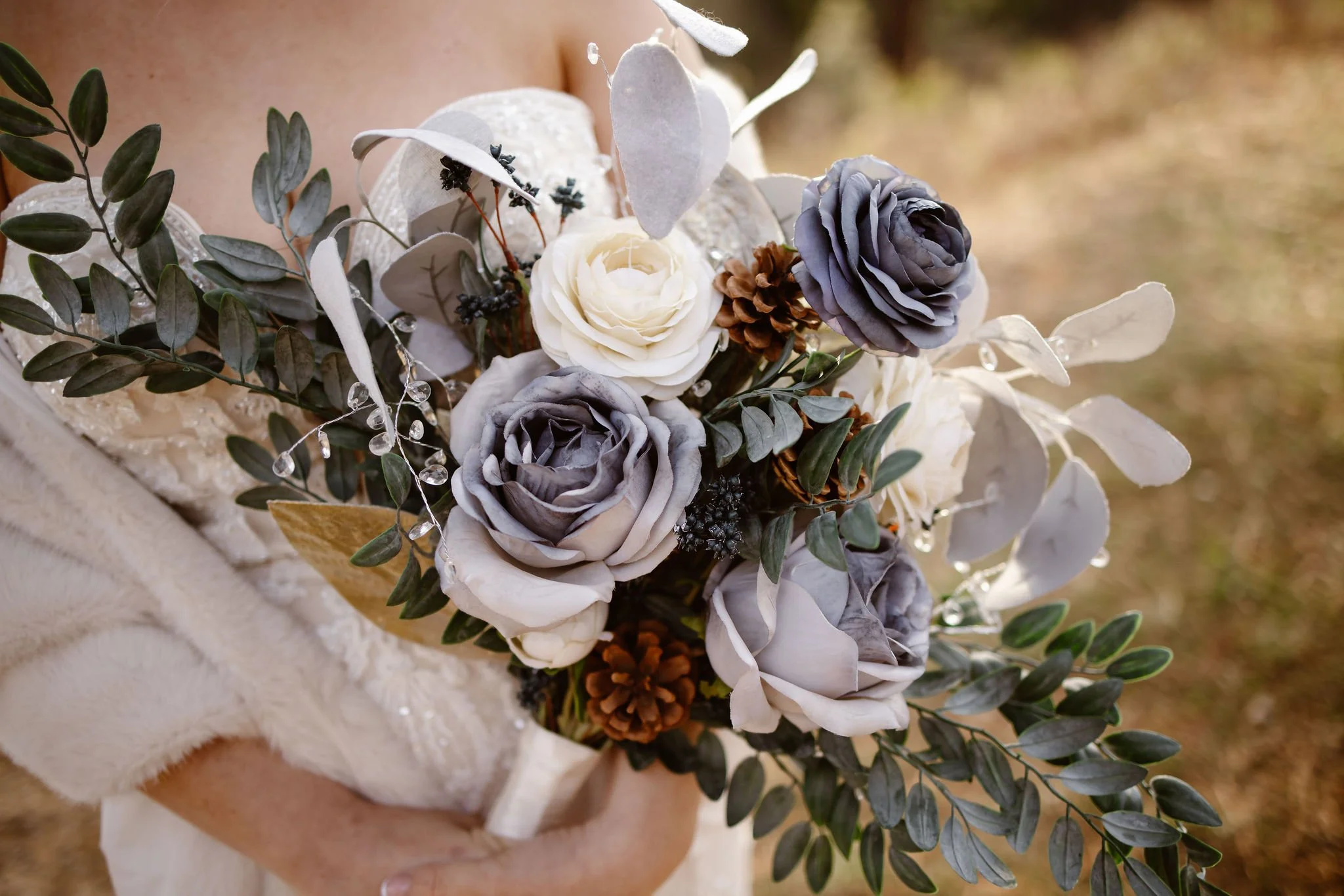 Close-up of a winter wedding bouquet with gray and white roses, eucalyptus, and pinecones held by a bride in a lace wedding dress, photographed by a Gatlinburg wedding photographer.