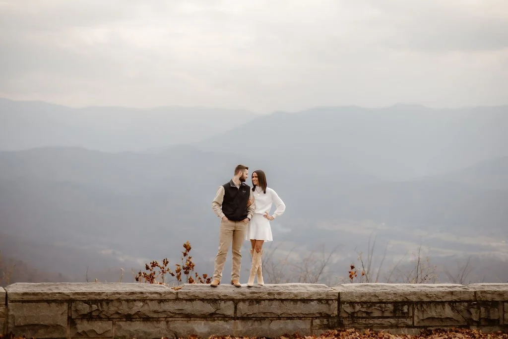 Couple standing on Foothills Parkway overlook wall with layered mountain views, wearing coordinated neutral engagement photos clothes captured by Gatlinburg photographer during fall engagement session