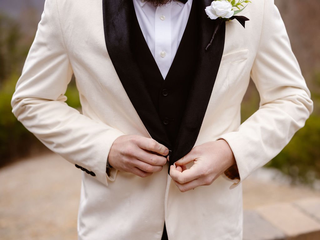 Groom adjusting his white tuxedo jacket with black shawl lapels during wedding portraits at Gatlinburg wedding cabins with Smoky Mountain scenery in the background.