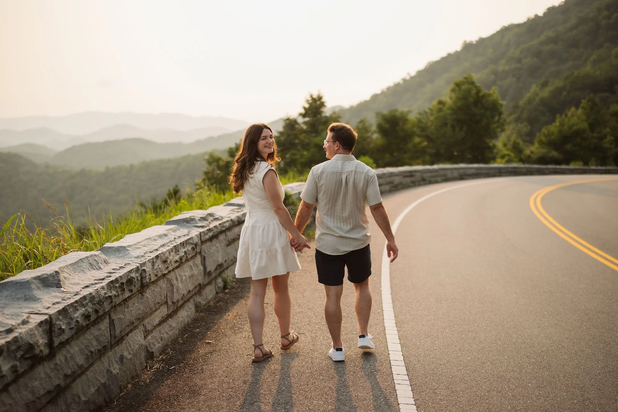 Couple walking hand in hand along a scenic mountain road during their smoky mountain engagement, captured at golden hour by a Gatlinburg photographer.
