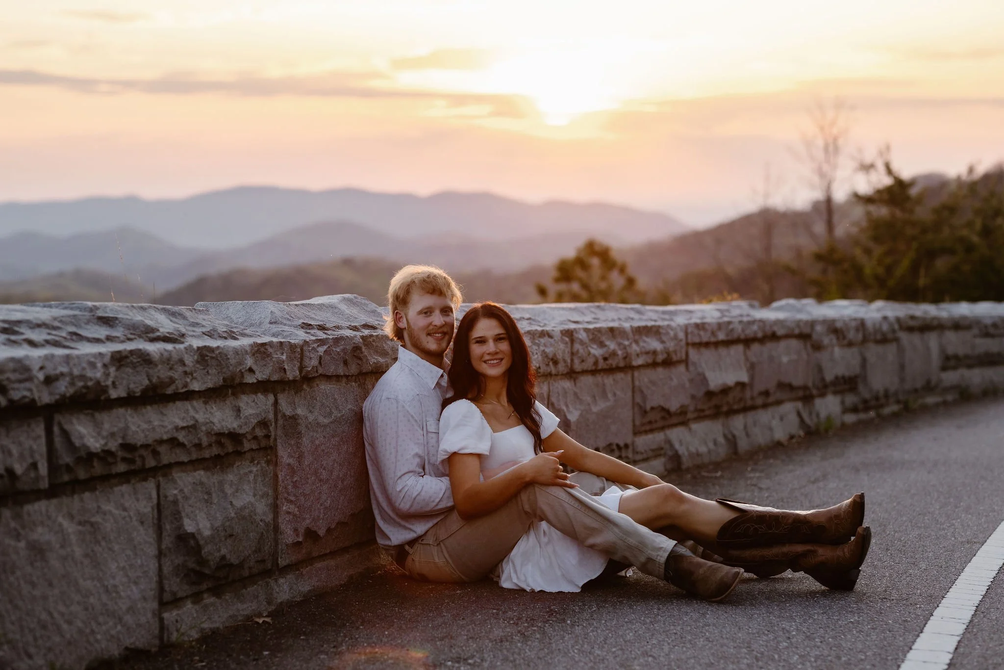Engaged couple sitting together at a scenic overlook during a sunset engagement with the Smoky Mountains glowing in the background