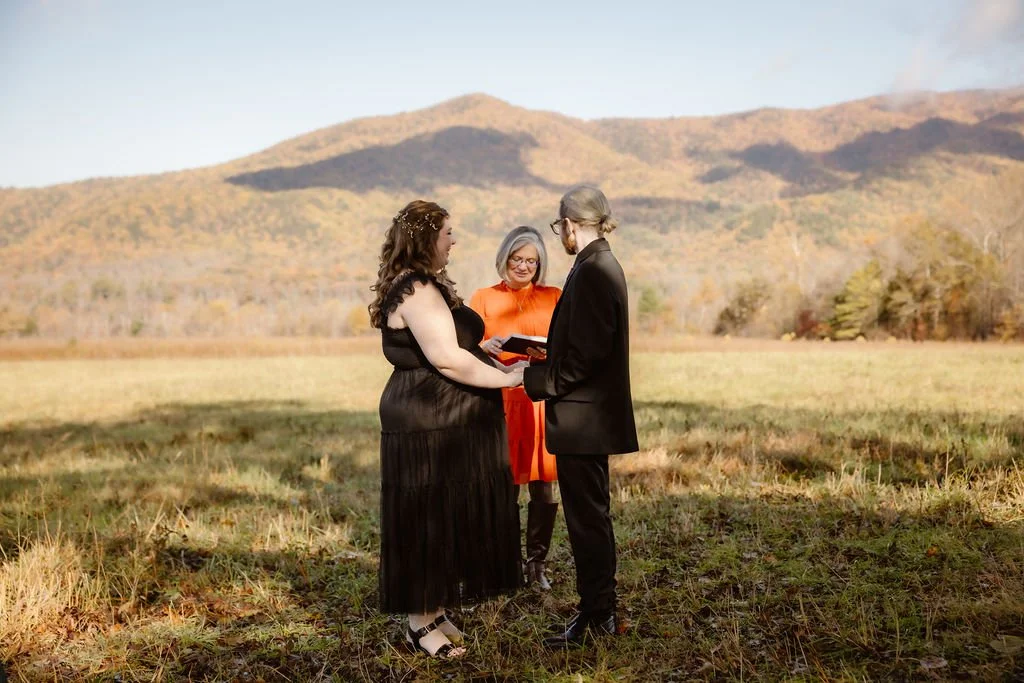 Wide outdoor Halloween Wedding ceremony in Smoky Mountains field, couple exchanging vows with officiant, Gatlinburg photographer capturing intimate fall elopement with mountain backdrop, autumn colors, and rustic countryside setting