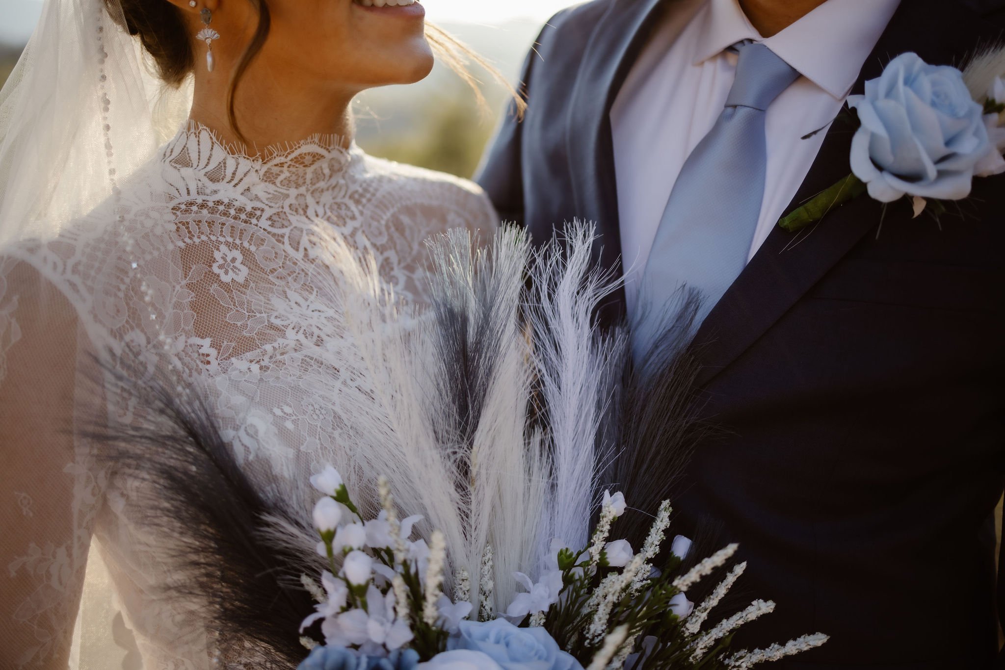 Close-up of bride’s lace wedding gown and bouquet of blue roses, white florals, and pampas grass, beside the groom in a navy suit with a light blue boutonnière, captured by National Park Photographers at Foothills Parkway in the Smoky Mountains.
