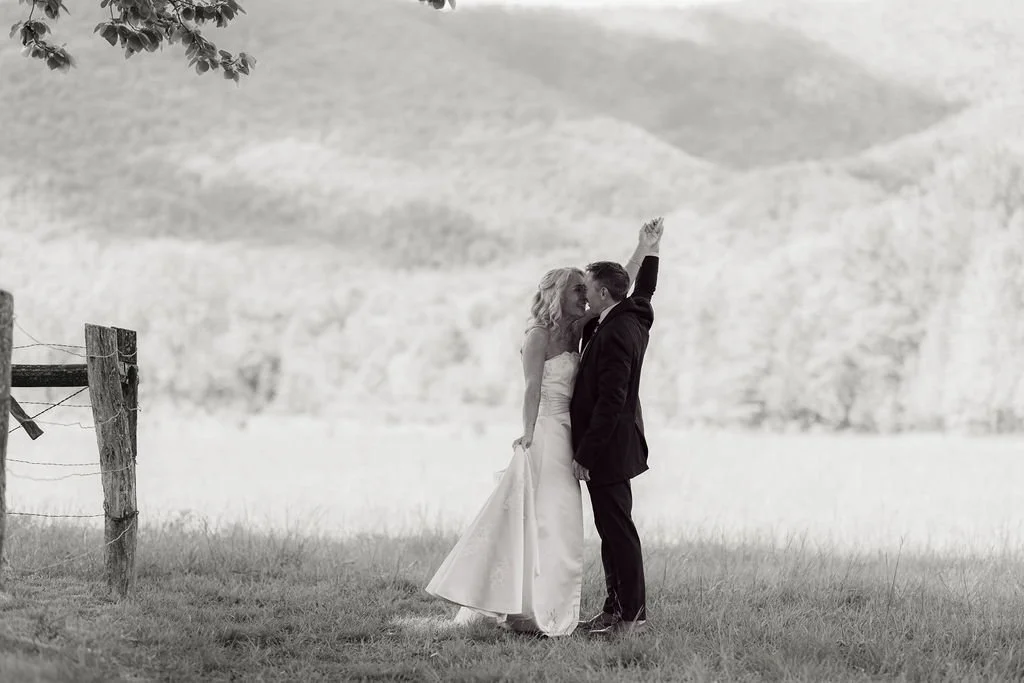 Black-and-white portrait of a newlywed couple kissing beside a rustic fence with the Smoky Mountains behind them during their Cades Cove gatlinburg elopement.