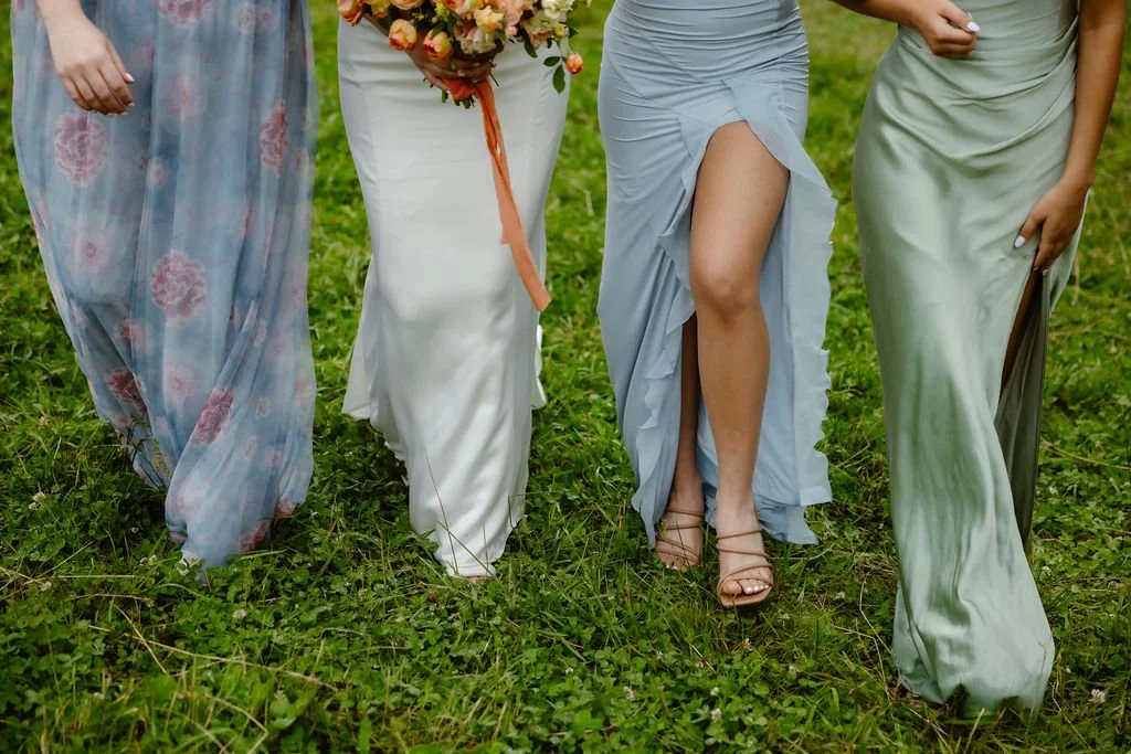 Close-up of the bride and bridesmaids walking through grass, showcasing flowing pastel dresses and the bride’s spring bouquet—stylish detail from Smoky Mountain Elopements in the Spring, photographed by a Gatlinburg photographer.