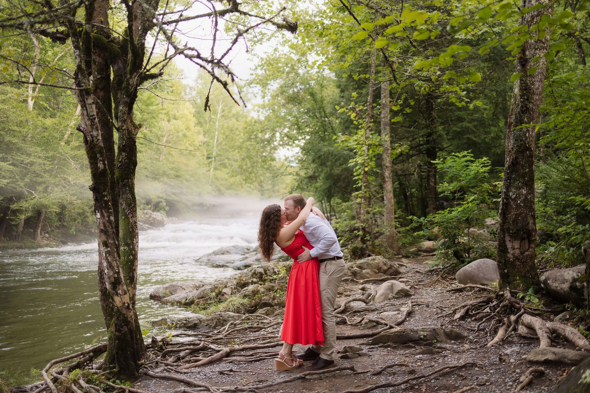 Couple kisses beside a misty gatlinburg waterfall in greenbrier after their surprise proposal.
