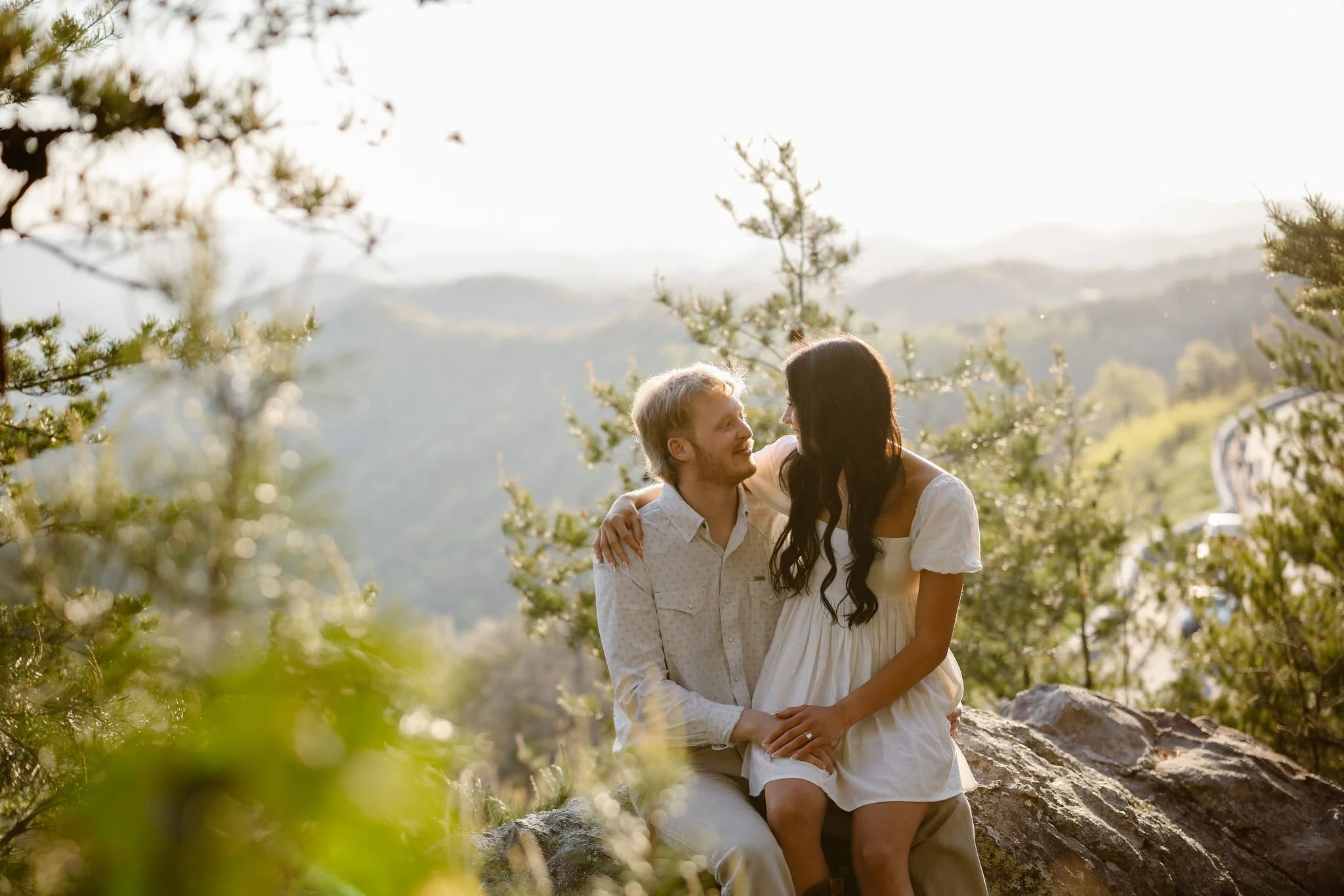 Newly engaged couple relaxing on a mountain overlook near Foothills Parkway with scenic Smoky Mountains views.
