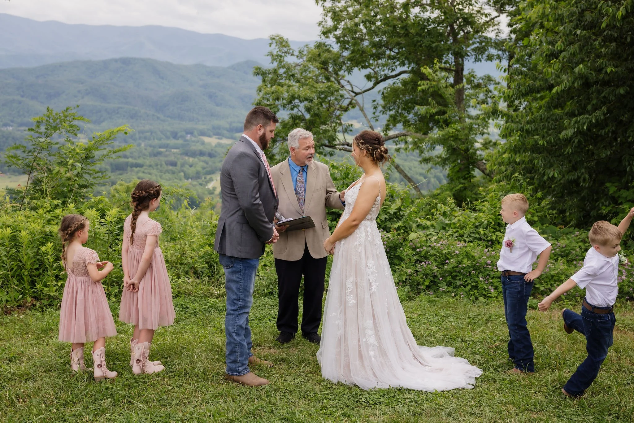 Bride and groom exchange vows surrounded by their four children during an intimate Gatlinburg elopement, with sweeping Smoky Mountain views and lush green trees framing their outdoor ceremony.