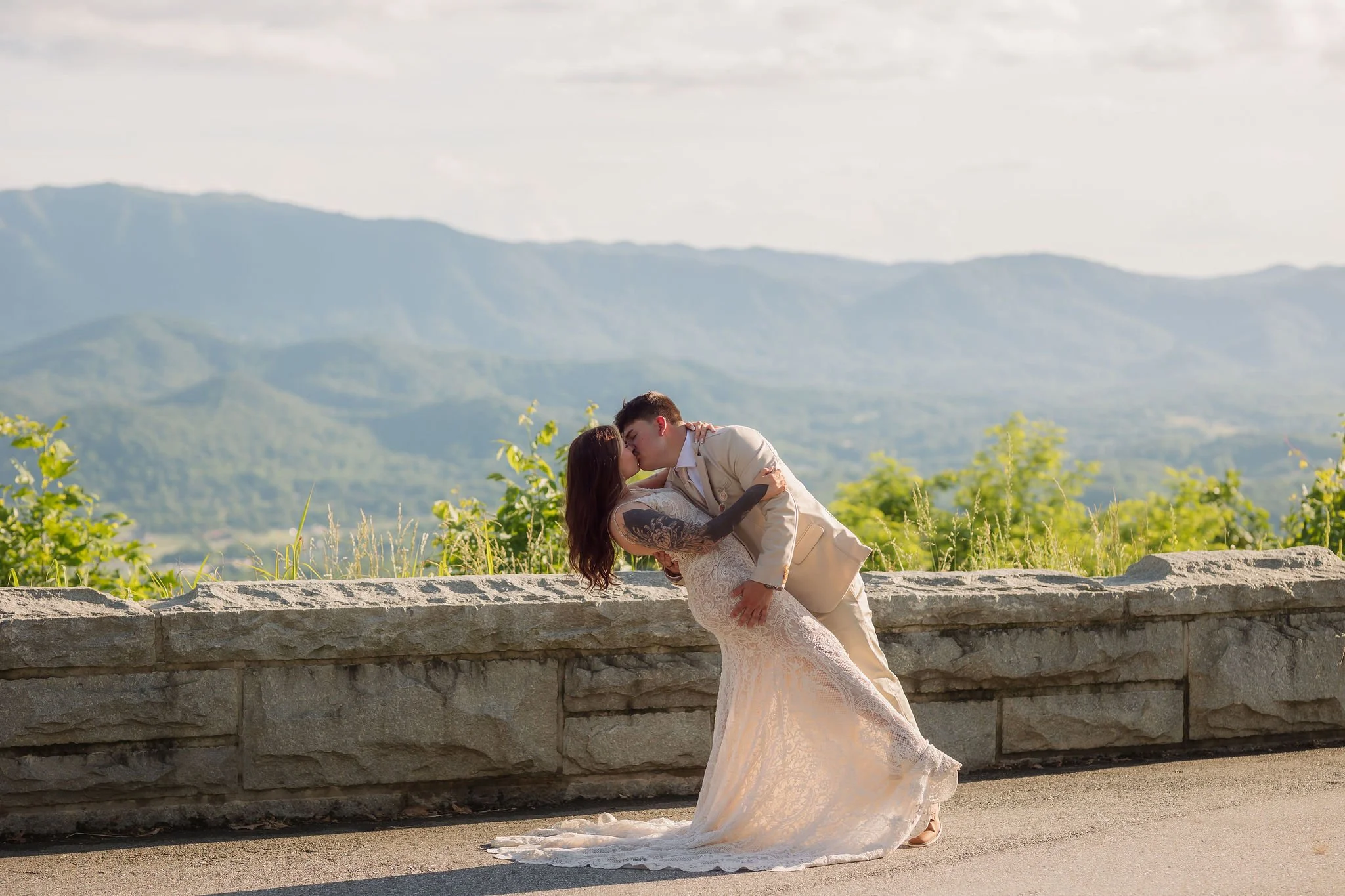Newlyweds share a dramatic dipped kiss along Foothills Parkway, surrounded by soft golden sunlight and layered mountain views, a romantic moment for couples visiting the Smokies.