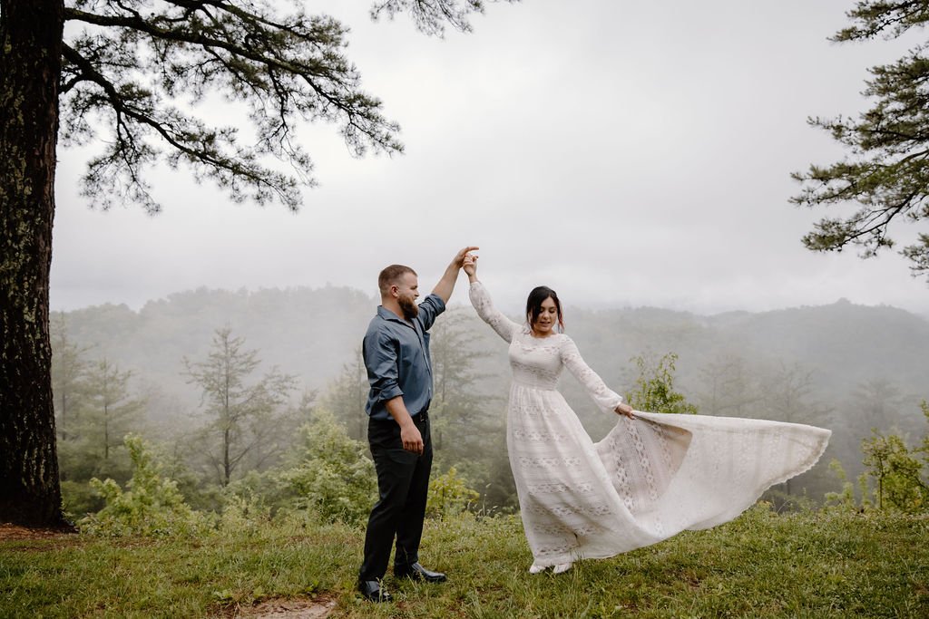 gatlinburg wedding with bride and groom dancing together on an outlook with thick fog and trees behind the bride and groom as the bride twirls in her gown captured by photographers in gatlinburg tn