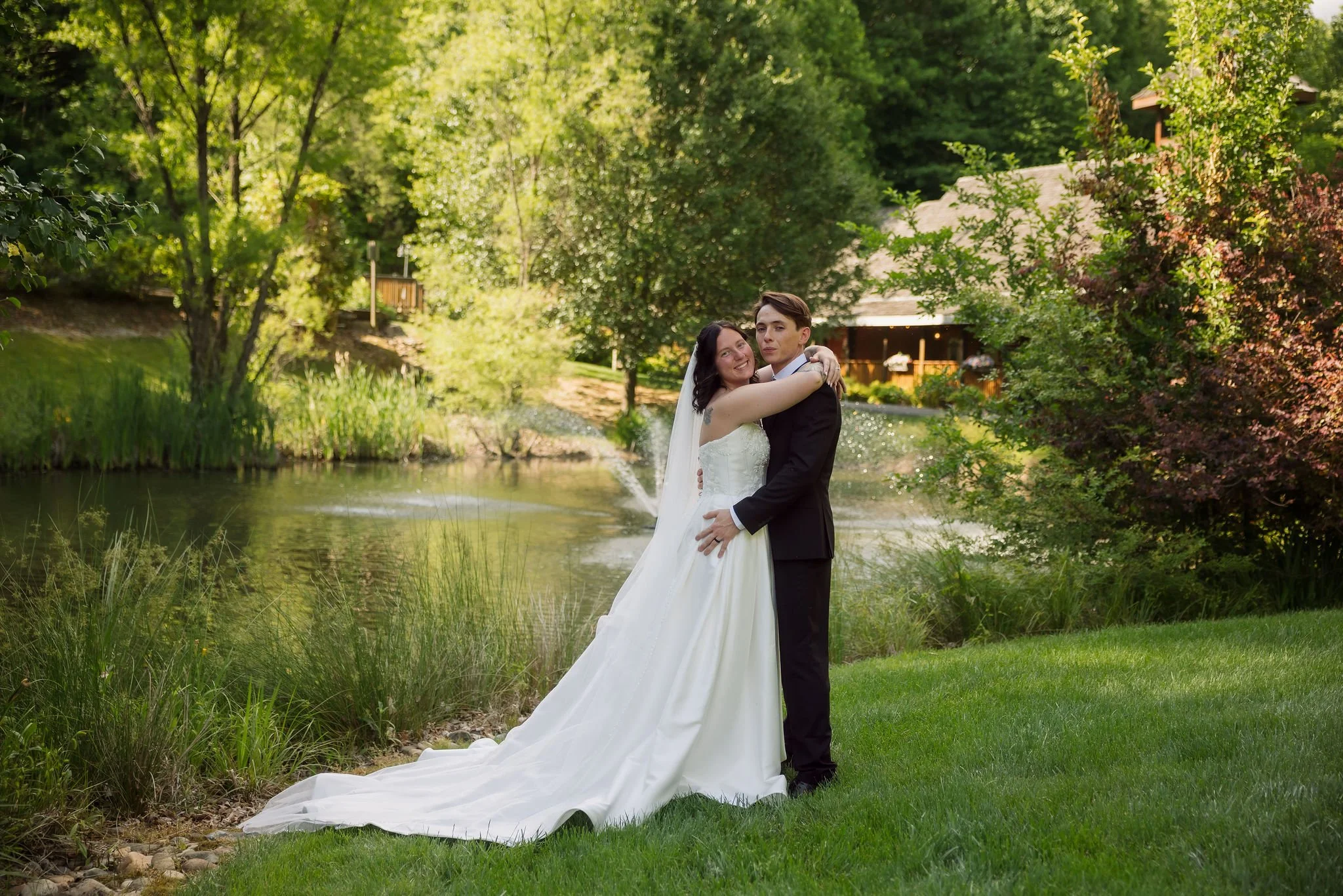 Newlyweds embrace beside a landscaped pond and fountain at the Little Log Chapel in Gatlinburg, surrounded by lush greenery after their Gatlinburg elopement.
