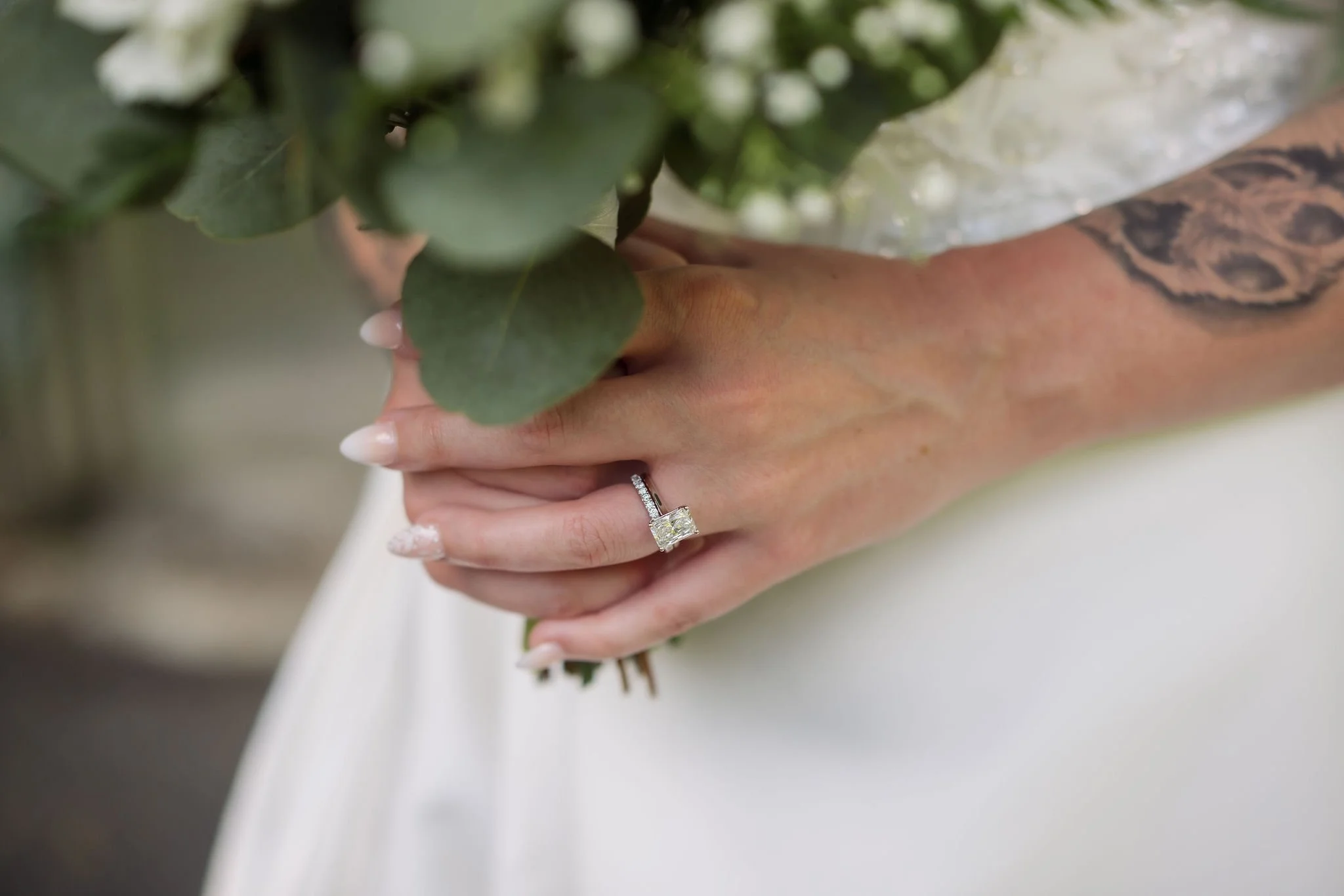 Close-up of the bride’s engagement ring and tattooed arm as she holds her greenery-filled bouquet during a Gatlinburg elopement.