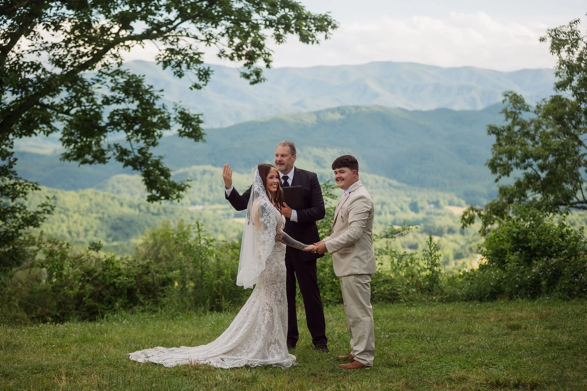 A couple exchanges vows beneath leafy trees with sweeping mountain views as their officiant leads an intimate outdoor wedding ceremony near Gatlinburg, Tennessee.