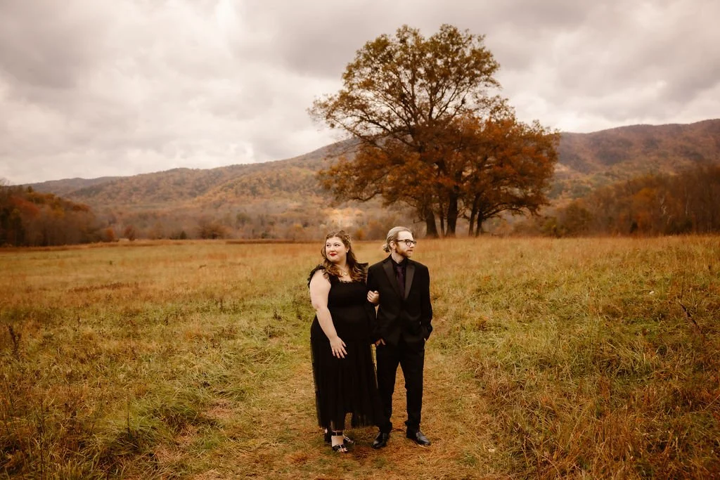 Couple standing together in open field during Halloween Wedding in Cades Cove, Gatlinburg photographer capturing romantic fall elopement with mountain backdrop, dramatic sky, and autumn foliage in Smoky Mountains