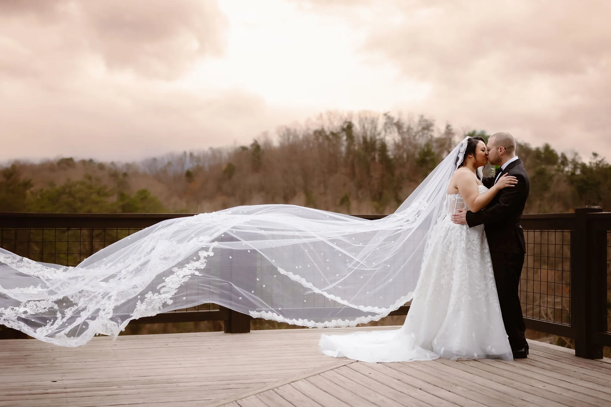 Bride and groom sharing a kiss on the deck at a Wild Briar Lodge Wedding, with the bride's flowing veil extending across the deck, captured by a Gatlinburg photographer during an Indoor elopement.