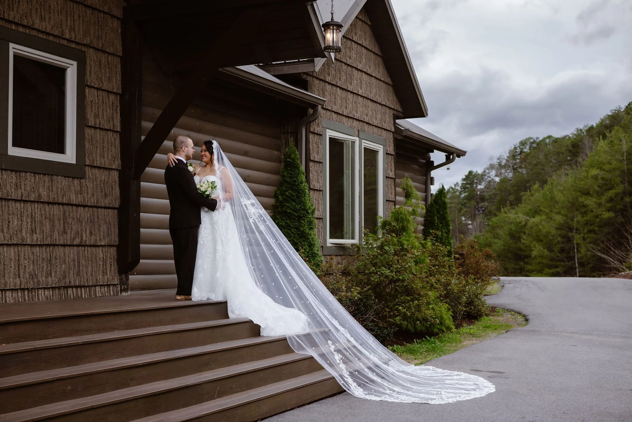 Bride and groom embrace on the lodge steps with the bride's long veil flowing behind her during a Wild Briar Lodge Wedding, captured by a Gatlinburg photographer during their Indoor elopement.
