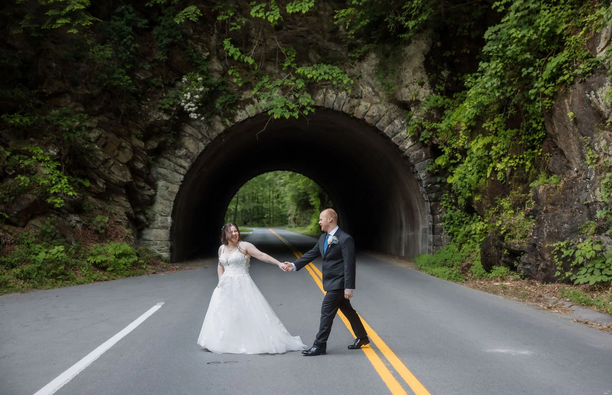 Bride and groom hold hands in front of a stone tunnel surrounded by lush forest during their Smoky Mountains gatlinburg elopement.