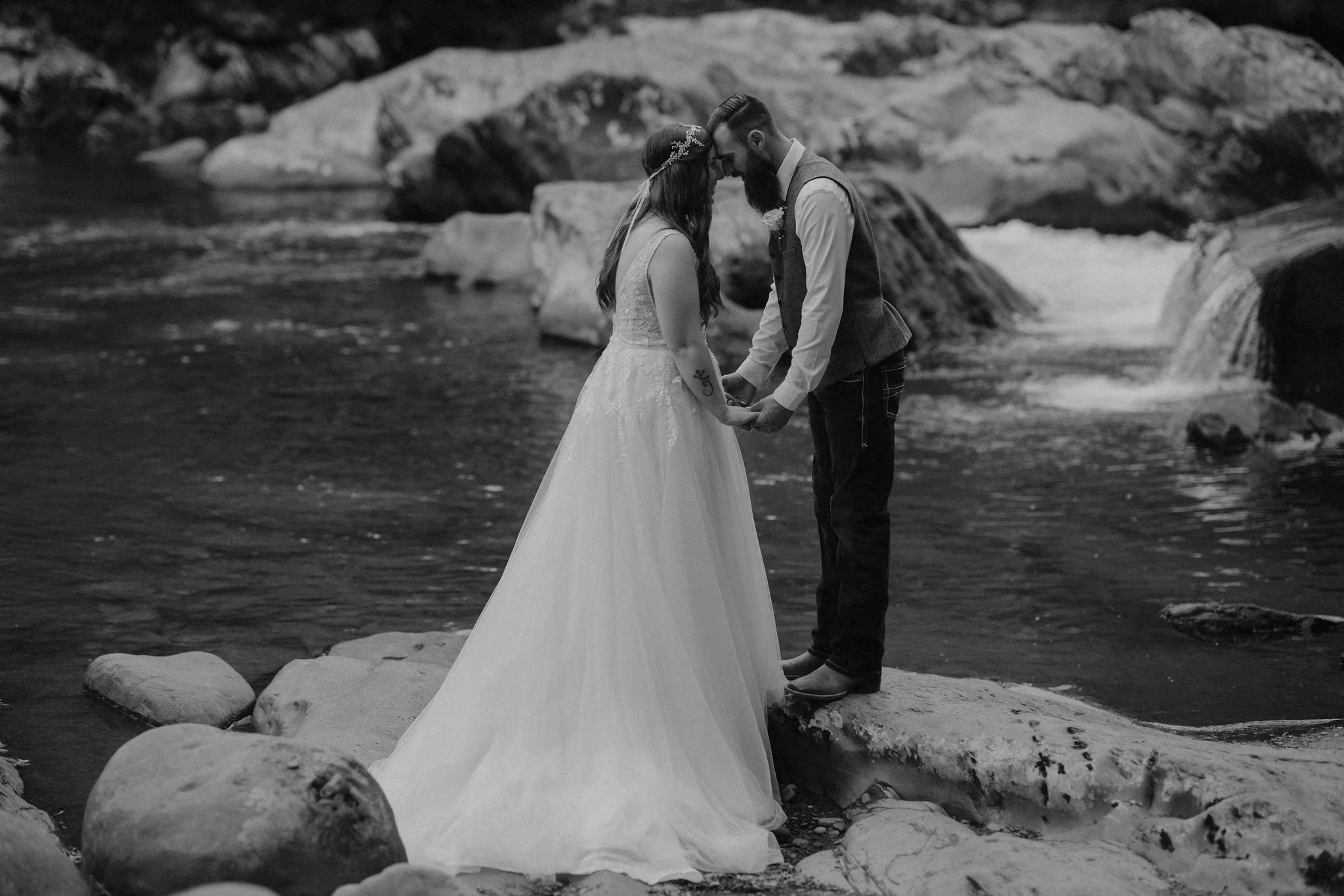 A bride and groom hold hands on the riverside rocks at Greenbrier in the Smoky Mountains during elopement photography, captured by a Gatlinburg wedding photographer.